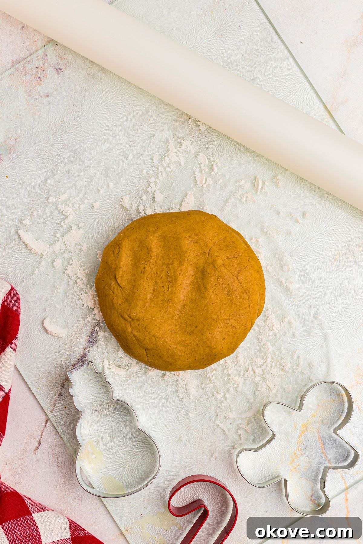 Festive Gingerbread Delights 7 Golden round disc of gingerbread cookie dough, with cookie cutters and rolling pin on marble table.