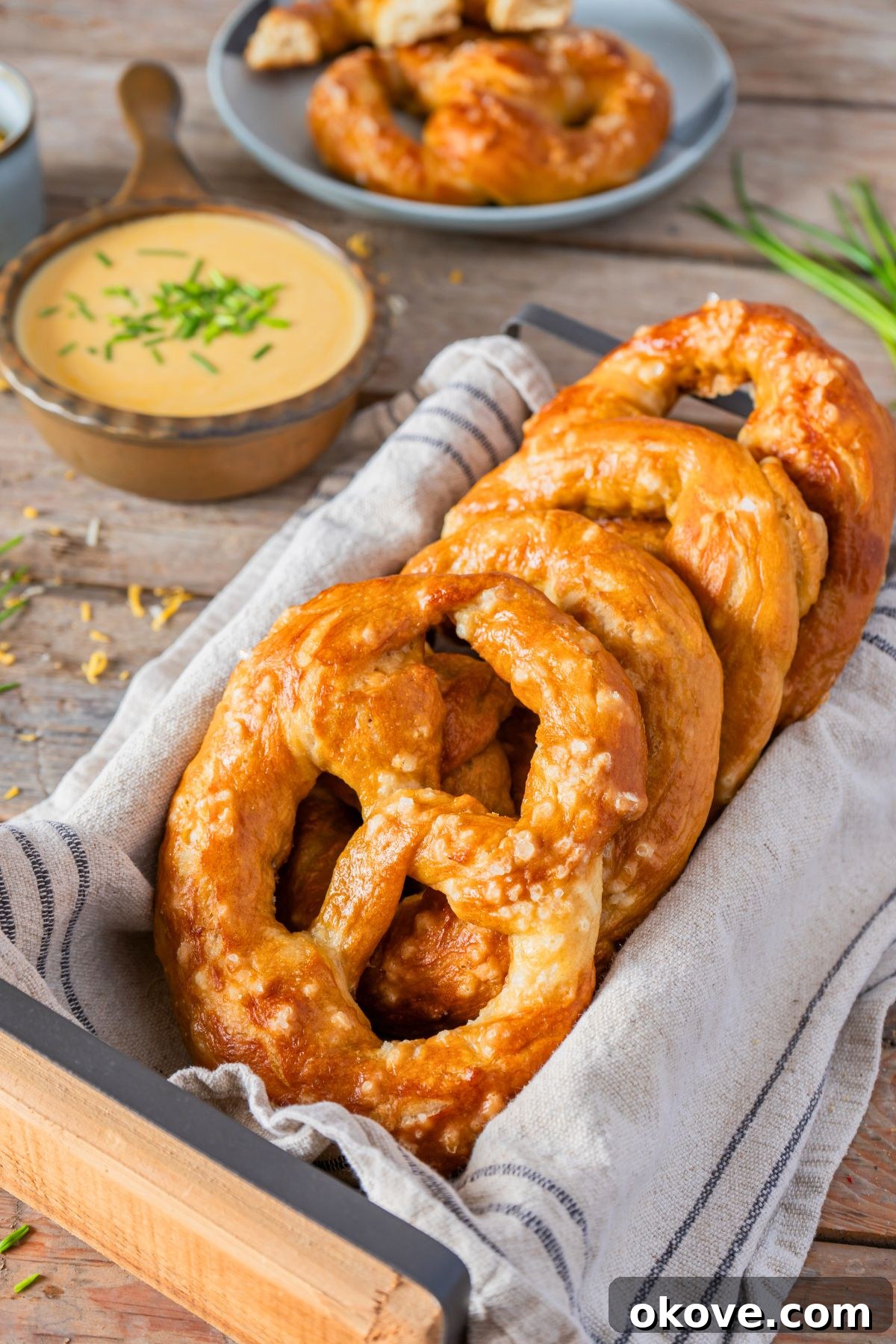 Pillowy Soft Pretzels 2 Golden baked soft pretzels stacked in a bread box, in front of cheese dip.