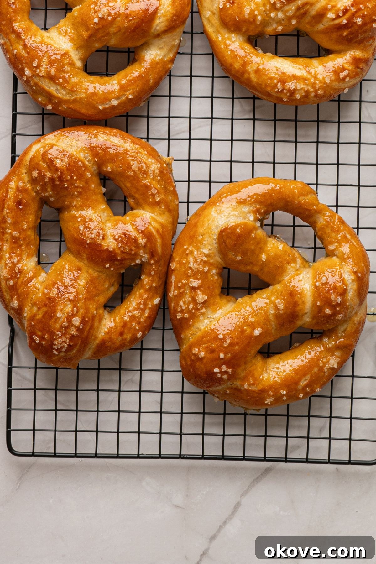 Pillowy Soft Pretzels 12 Baked golden pretzels on a wire rack on a marble table.