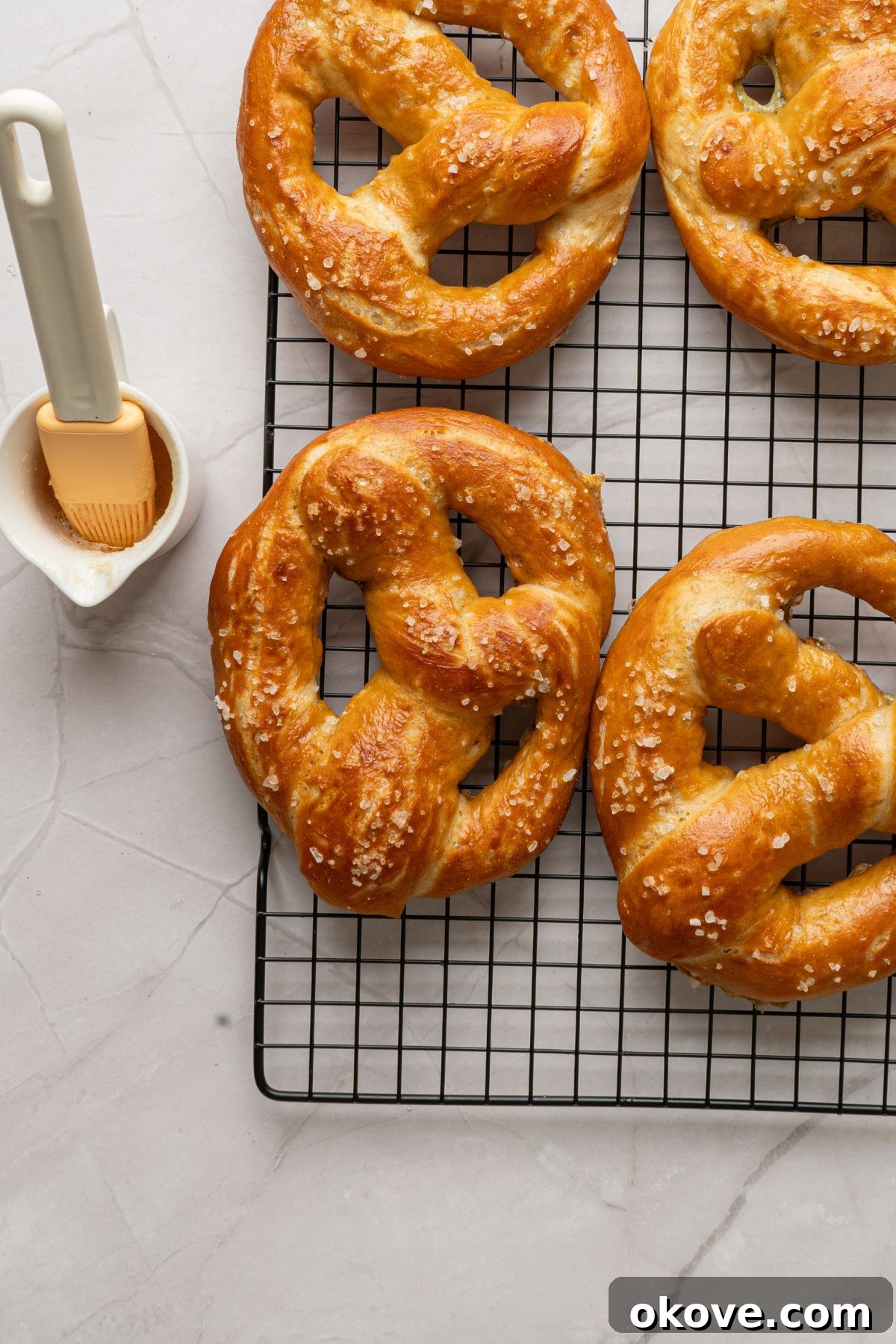 Pillowy Soft Pretzels 13 Baked golden pretzels on a wire rack on a marble table being brushed with butter.