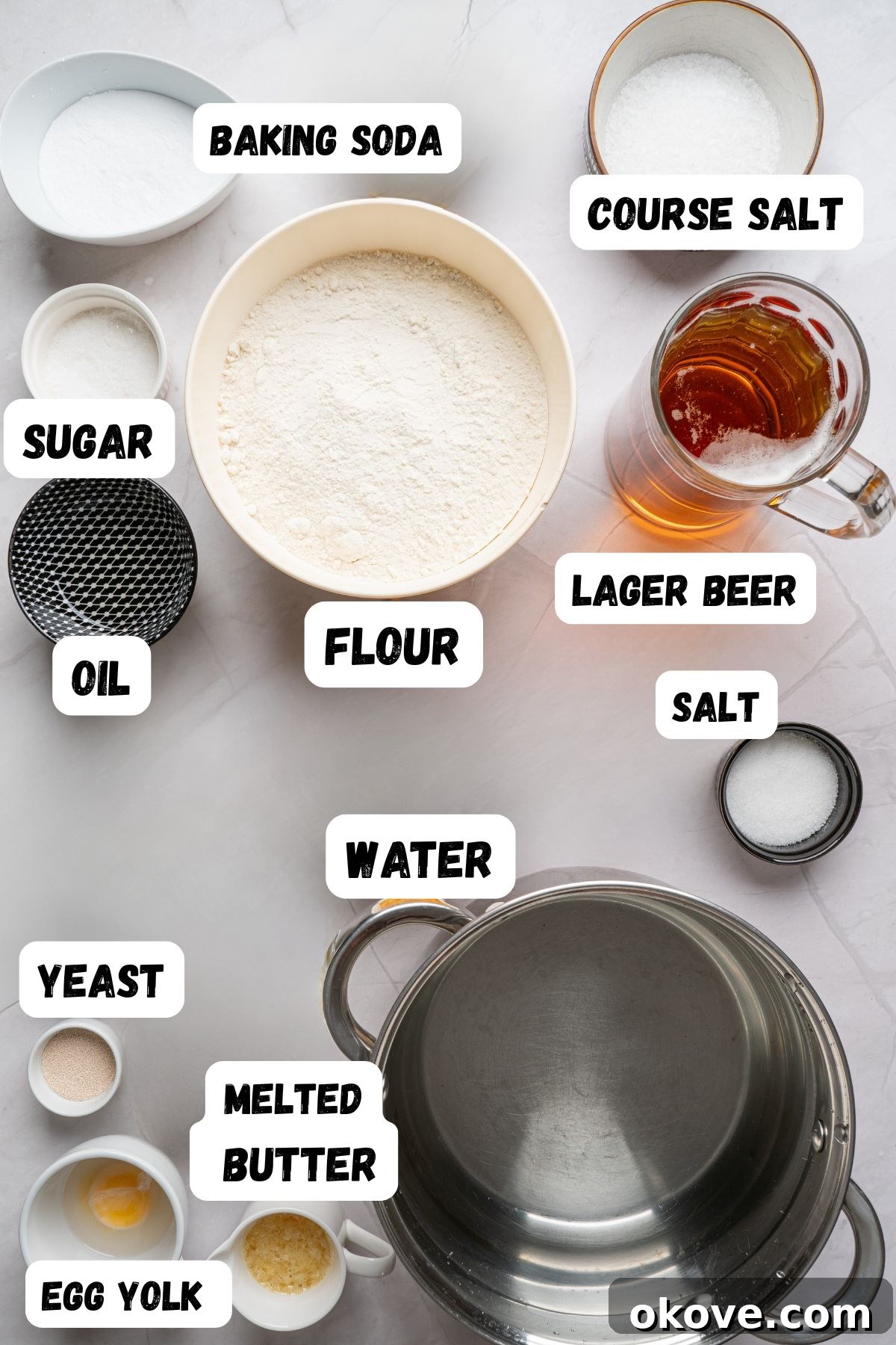 Pillowy Soft Pretzels 3 Soft pretzel ingredients like yeast, salt, and water, measured into small bowl on a white marble table, with labels of each ingredient printed over them.