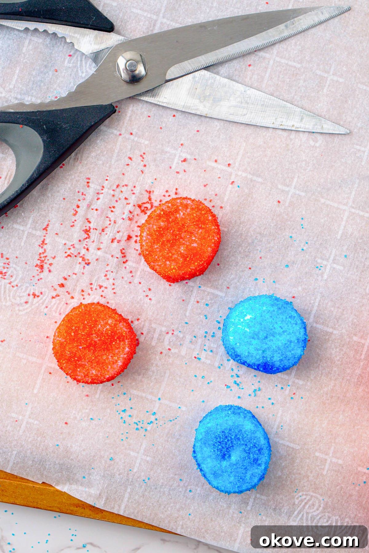 Red, White, and Gooey S'mores Dip 6 Red and blue sugar-coated marshmallows being carefully cut in half with kitchen shears on a cutting board.