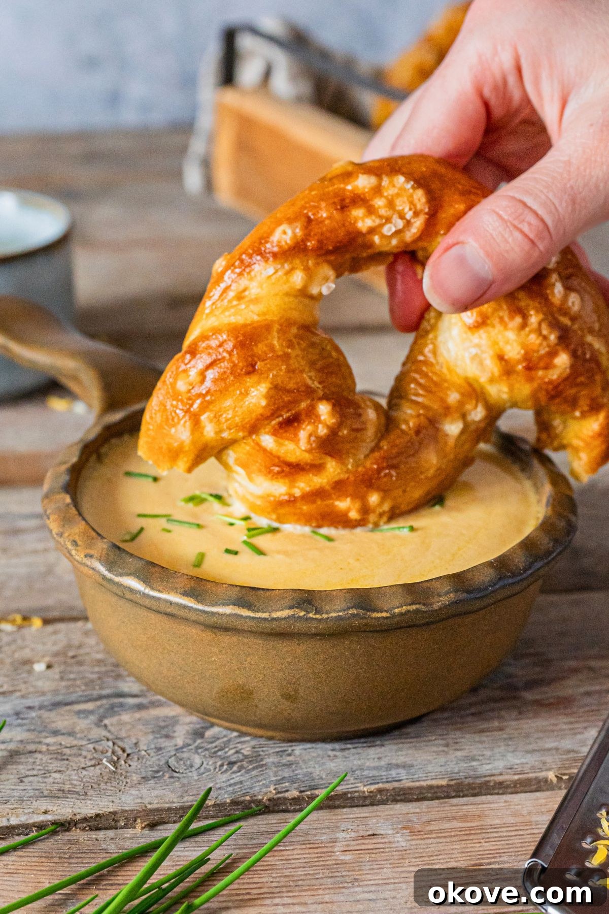 A small bowl of golden beer cheese dip with a freshly baked soft pretzel being enthusiastically dipped into the creamy cheese.