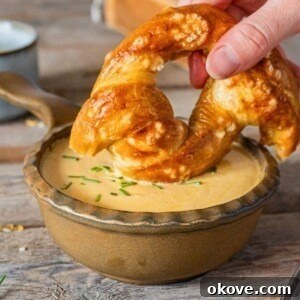 A small brown bowl with melted cheese dip, with a soft pretzel being dipped into the cheese.
