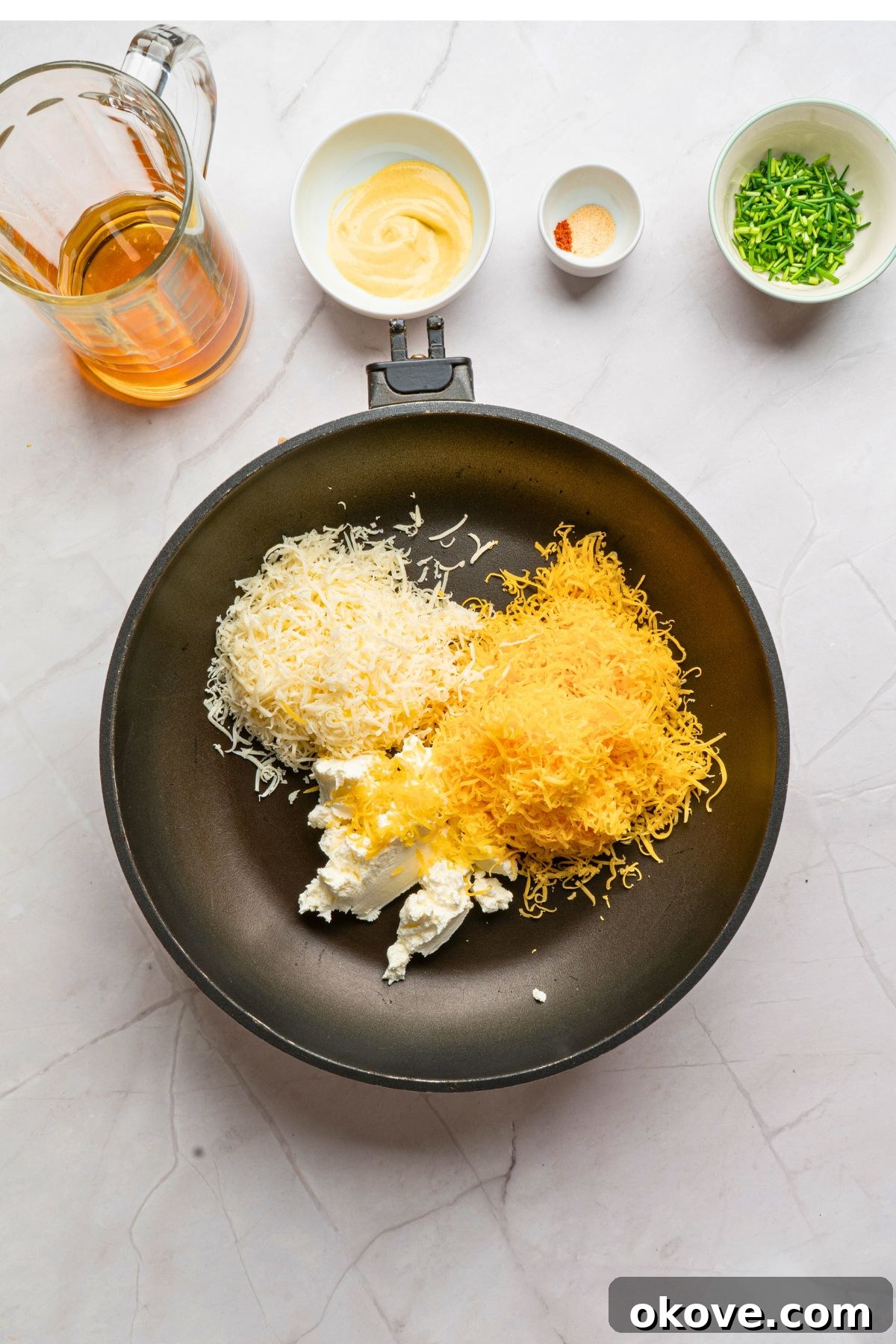 Softened cream cheese, freshly shredded sharp cheddar, and gouda being added to a medium saucepan over very low heat, meticulously arranged and ready to be gently melted together.