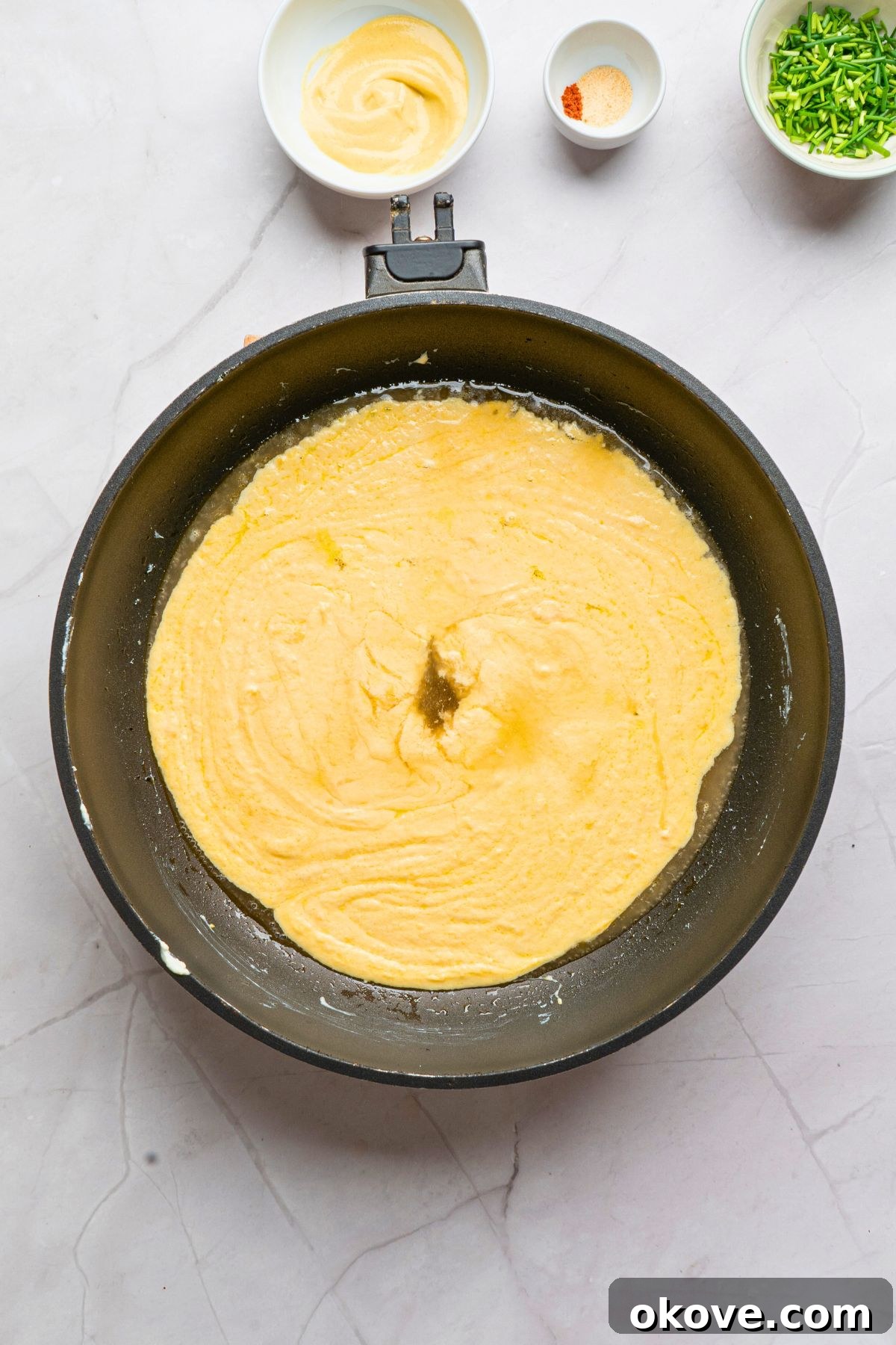 The melting cheeses are being diligently stirred in a saucepan as a light lager beer is gradually poured in to create a perfectly smooth, creamy texture without clumping.