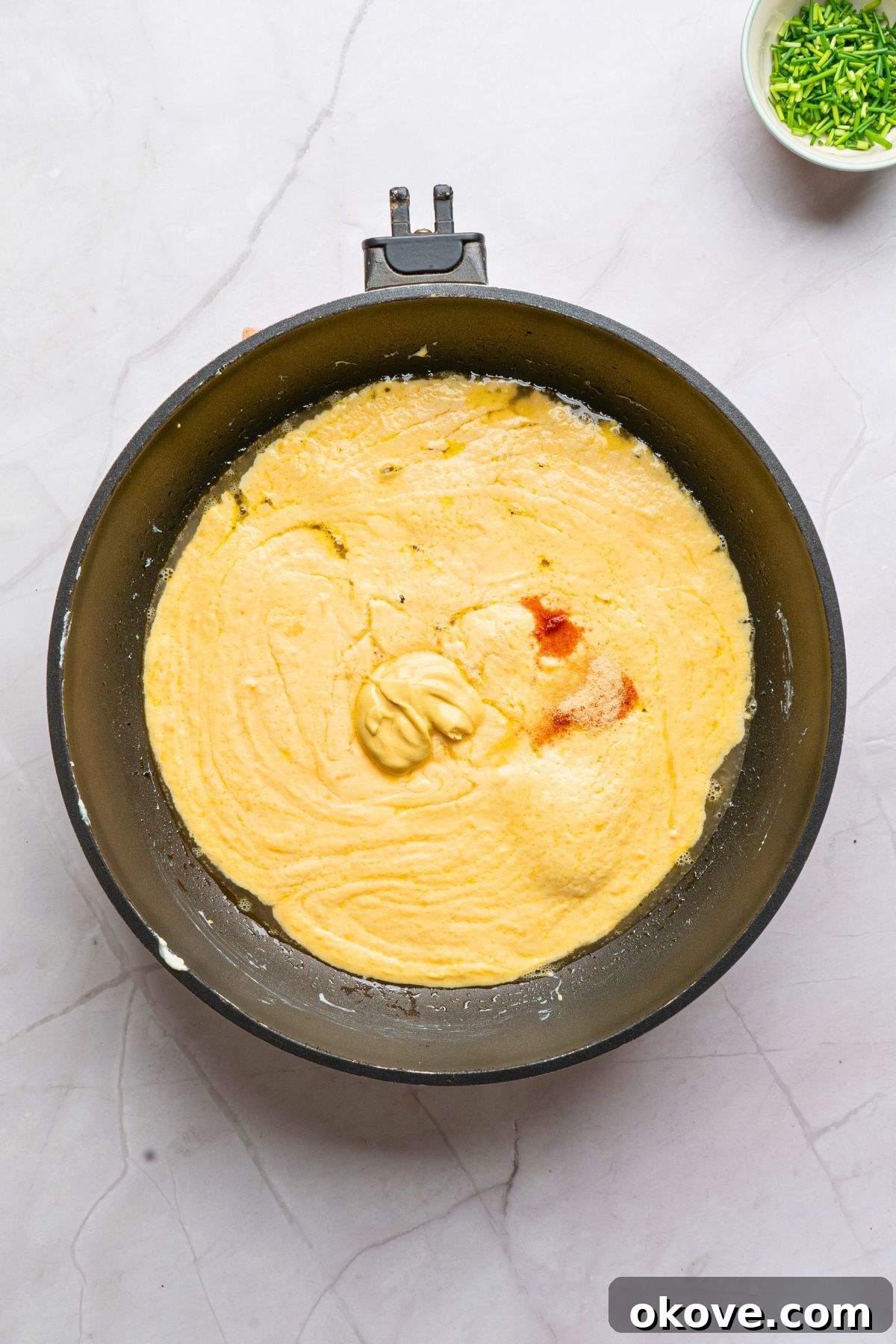 The beer cheese dip simmering gently in a saucepan, with Dijon mustard and garlic powder thoroughly stirred in, achieving a perfectly smooth and beautifully blended consistency.