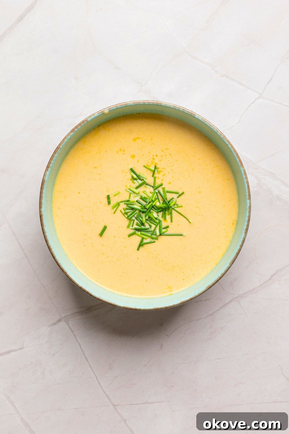 A small, elegant serving bowl filled with the freshly prepared beer cheese dip, artfully garnished with vibrant, freshly chopped chives, poised and ready to be enjoyed warm.