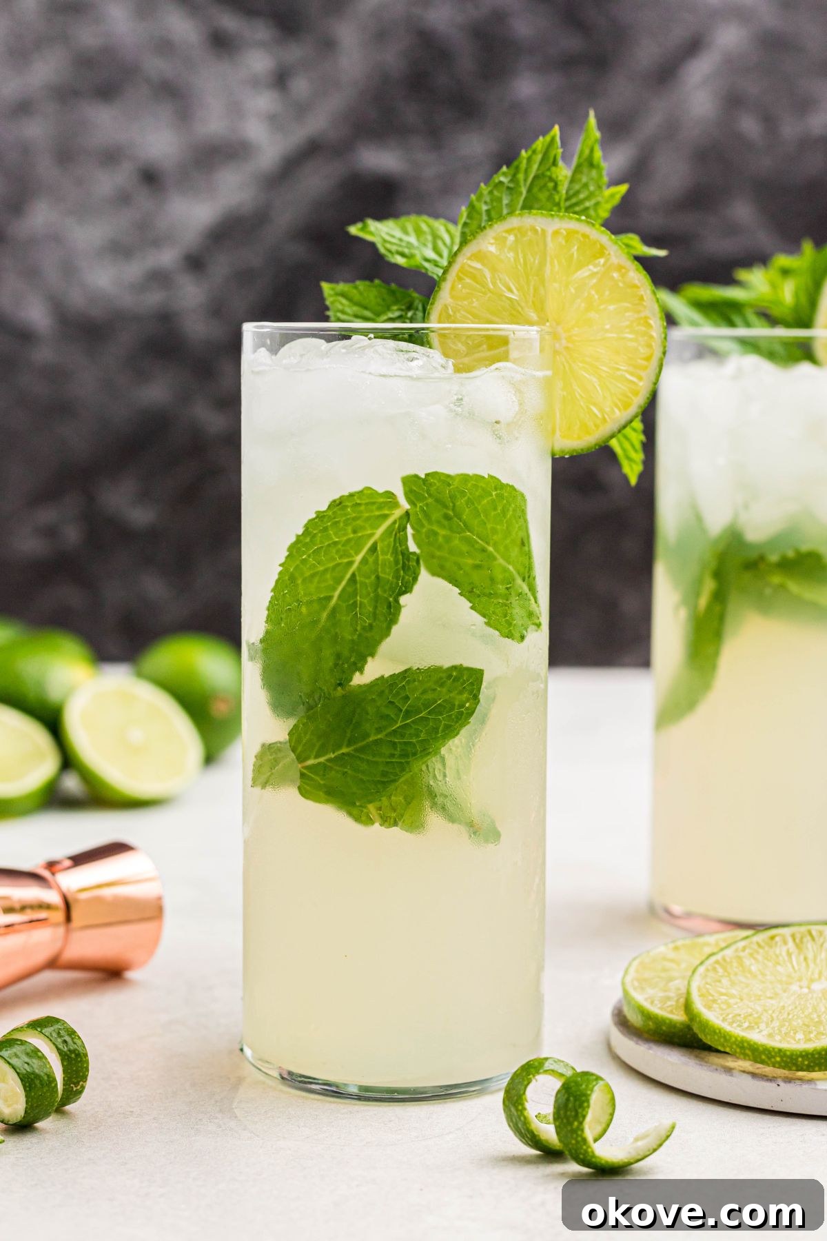 Bright yellow mojito drink in a tall chilled glass, garnished with lime slices and fresh mint, resting on a marble table with lime curls.