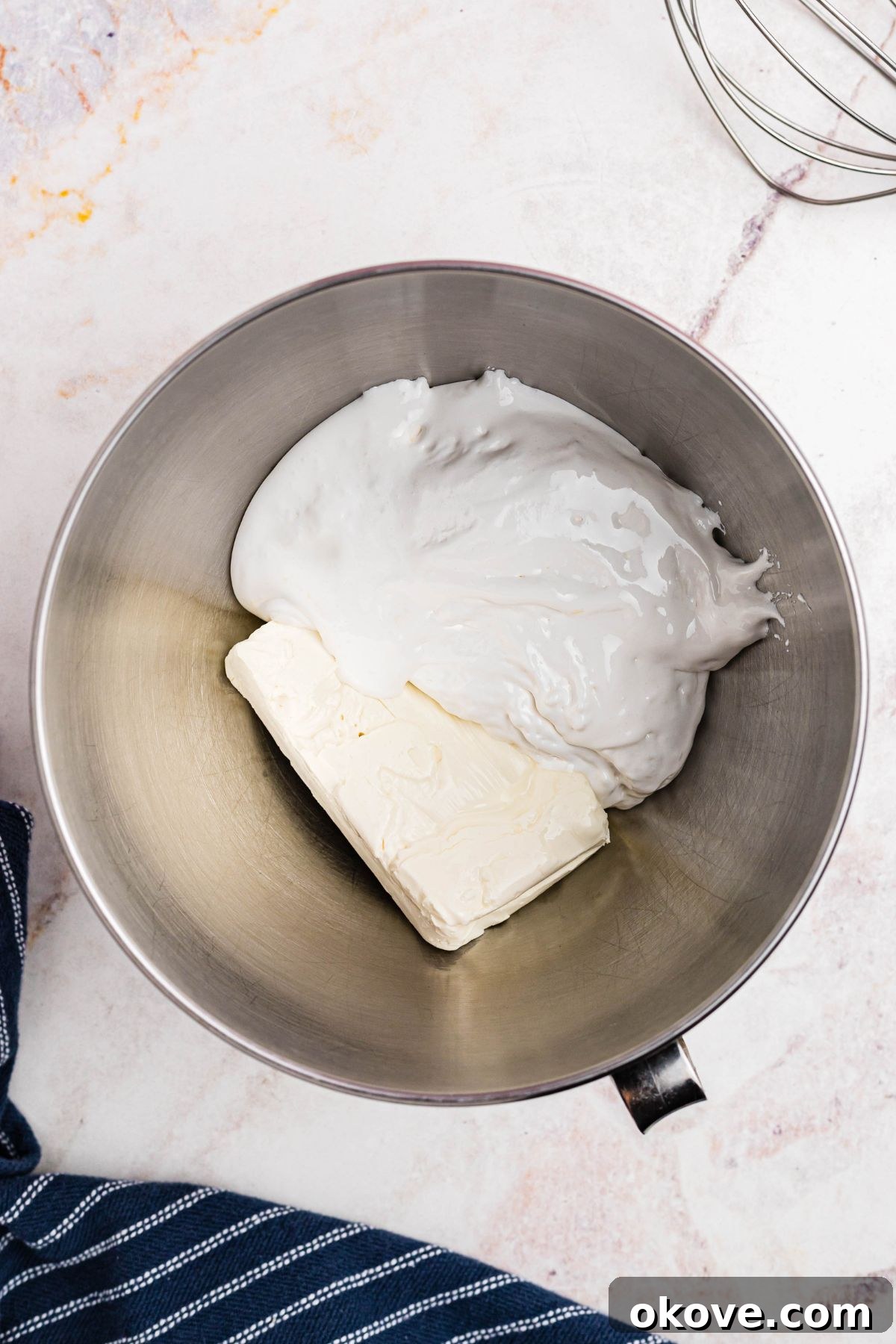 Sweet and Creamy Fruit Dip 4 A block of softened cream cheese and a generous scoop of sticky marshmallow creme are shown together in a gleaming silver mixing bowl, ready to be combined.