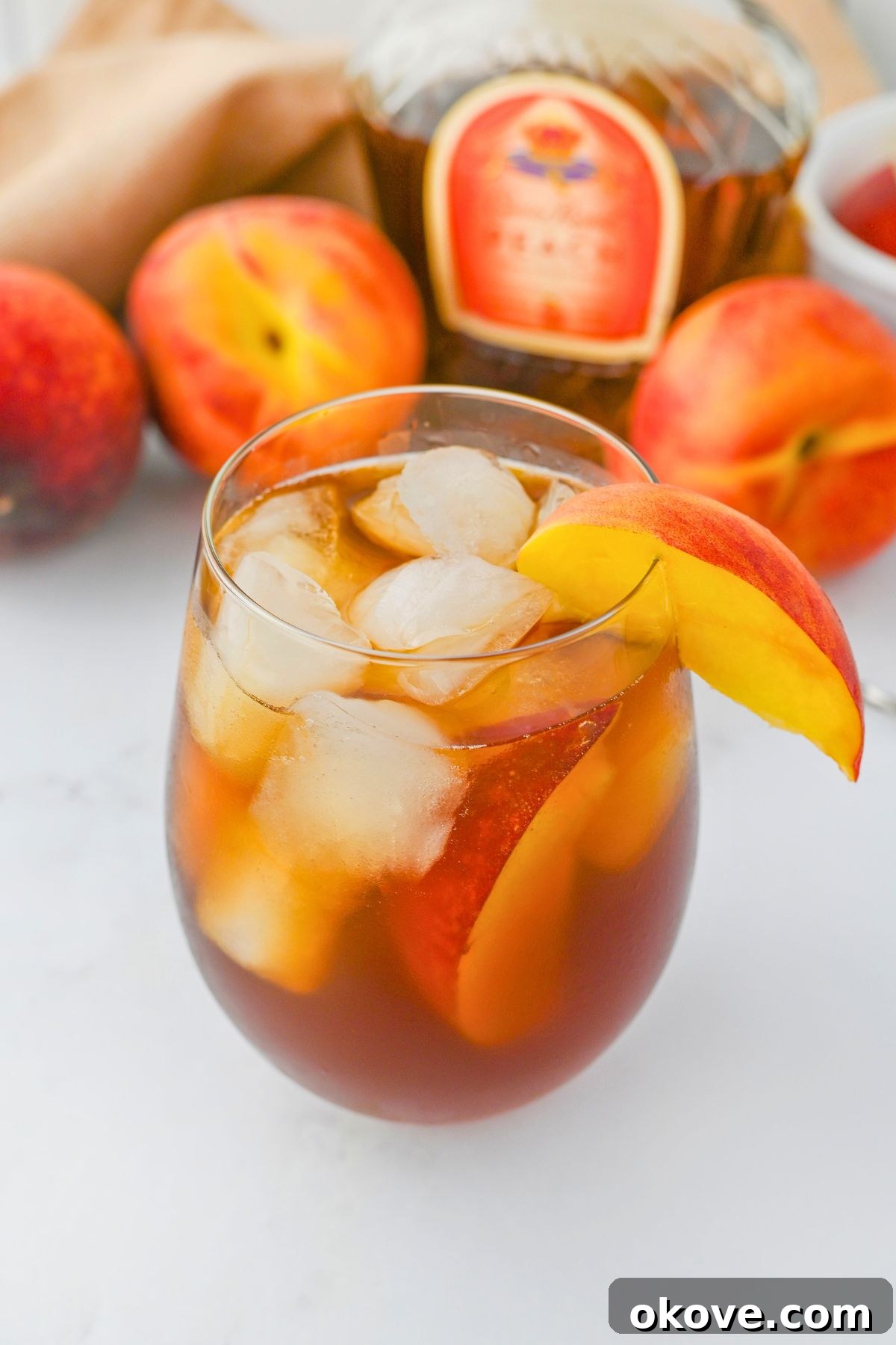 Imperial Peach Nectar 2 A chilled glass of Royal Peach Tea cocktail, garnished with a fresh peach slice, with ice and peach whiskey visible, ready to be enjoyed.