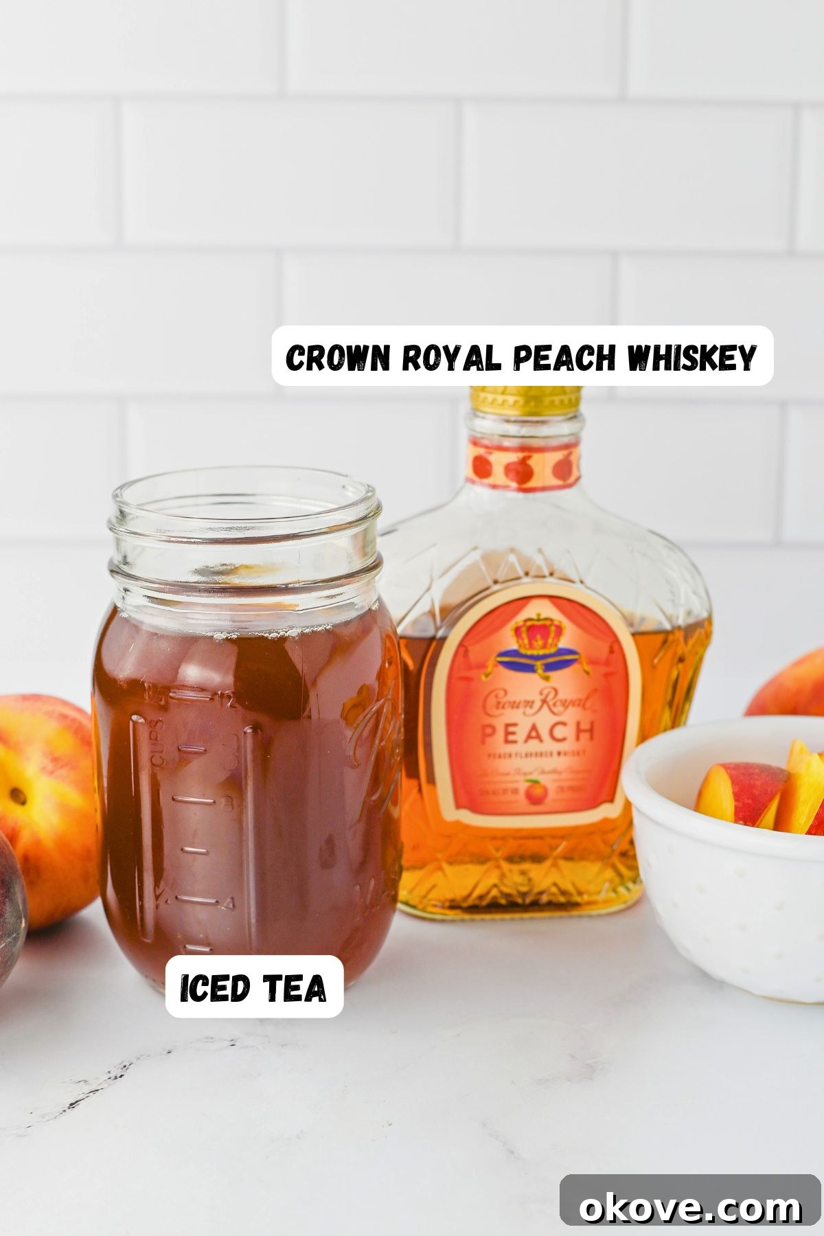 Imperial Peach Nectar 3 A bottle of Crown Royal Peach Flavored Whisky stands next to a mason jar filled with sweet iced tea, resting on a clean marble surface. Fresh peaches in a white bowl add a touch of color and natural beauty to the scene.