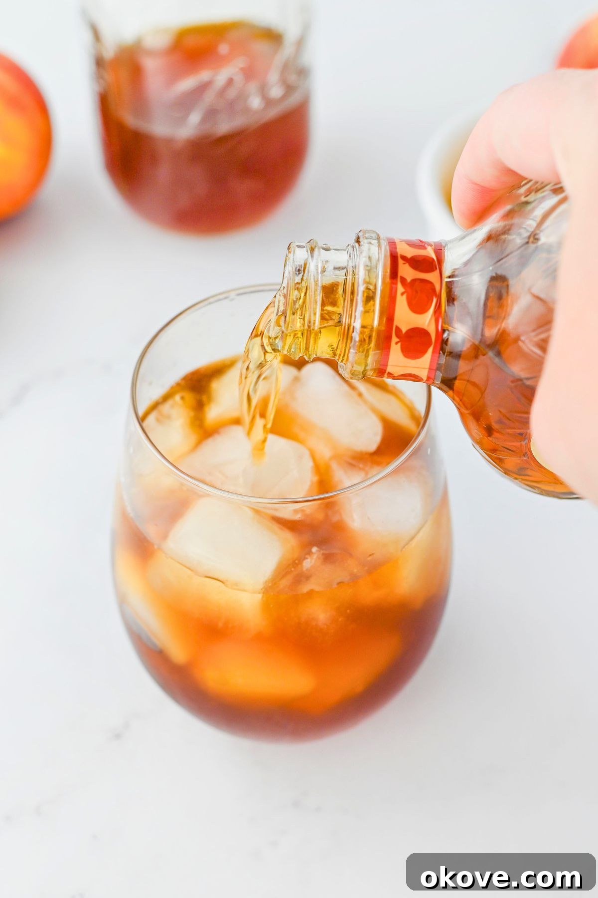 Imperial Peach Nectar 4 A hand pouring Crown Royal Peach whiskey into a glass filled with ice and sweet tea.