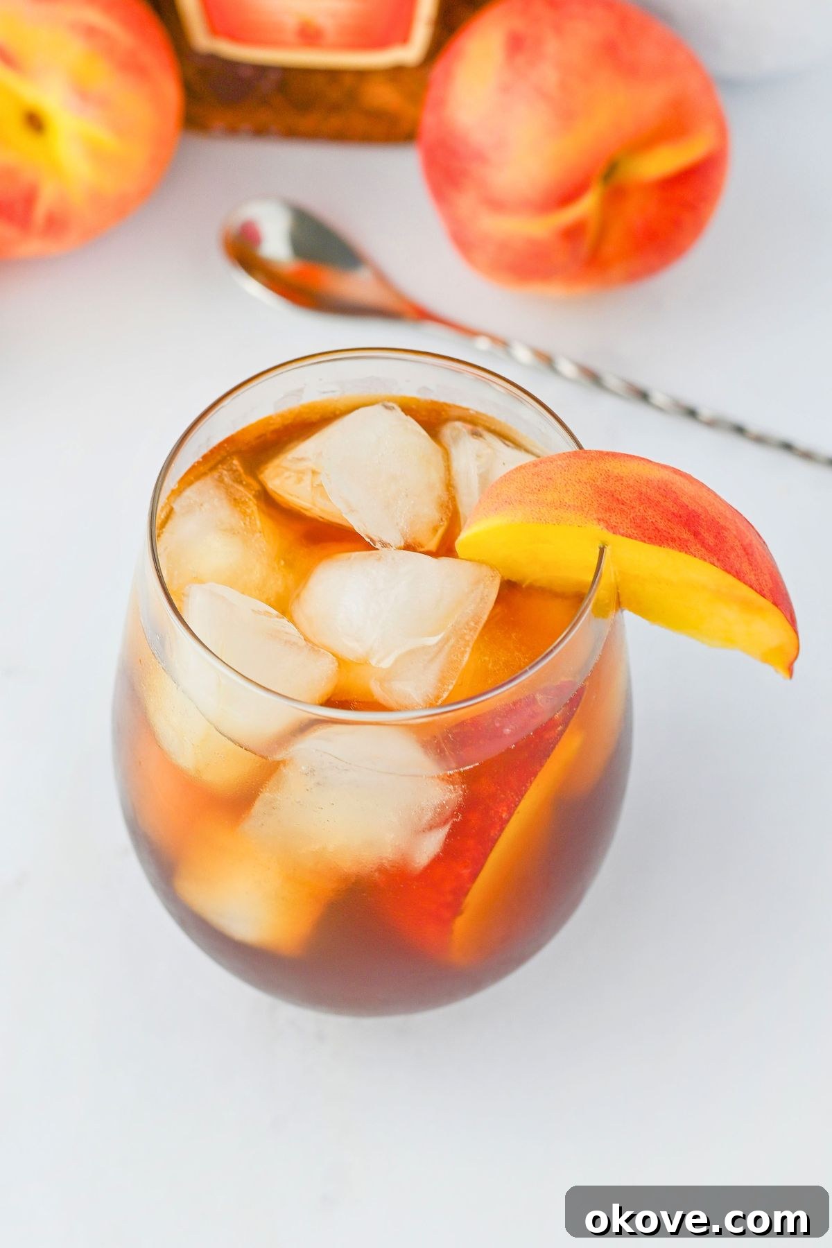 Imperial Peach Nectar 5 A finished Royal Peach Tea cocktail, complete with ice and a fresh peach slice garnish, sitting on a table.