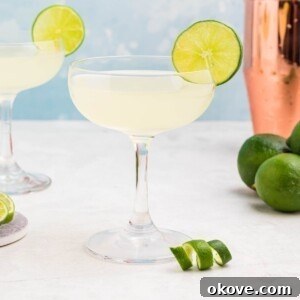 Tropical Rum Delight 7 Coupe glass filled with drink, garnished with lime wheel, on a marble table with a blue backdrop.