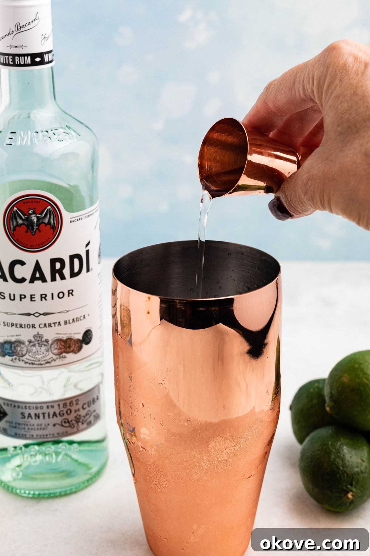 Tropical Rum Delight 4 Rum, simple syrup, and lime juice, being poured into a rose gold cocktail shaker.