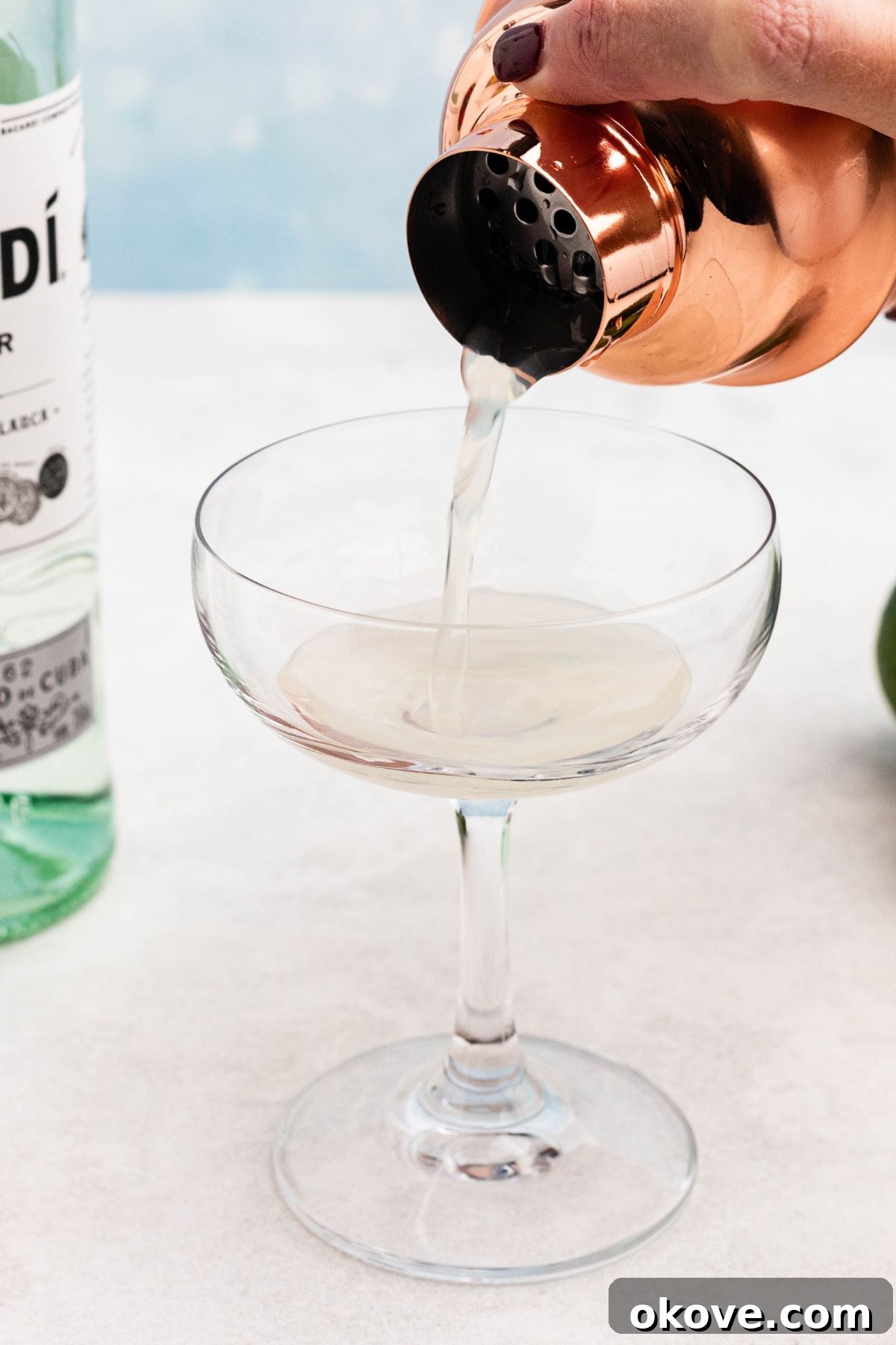 Tropical Rum Delight 5 Mixed ingredients being poured through a strainer on a cocktail shaker into a small coupe glass.