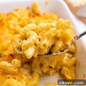 Spoonful of mac and cheese being lifted out of casserole dish, showcasing its creamy texture.