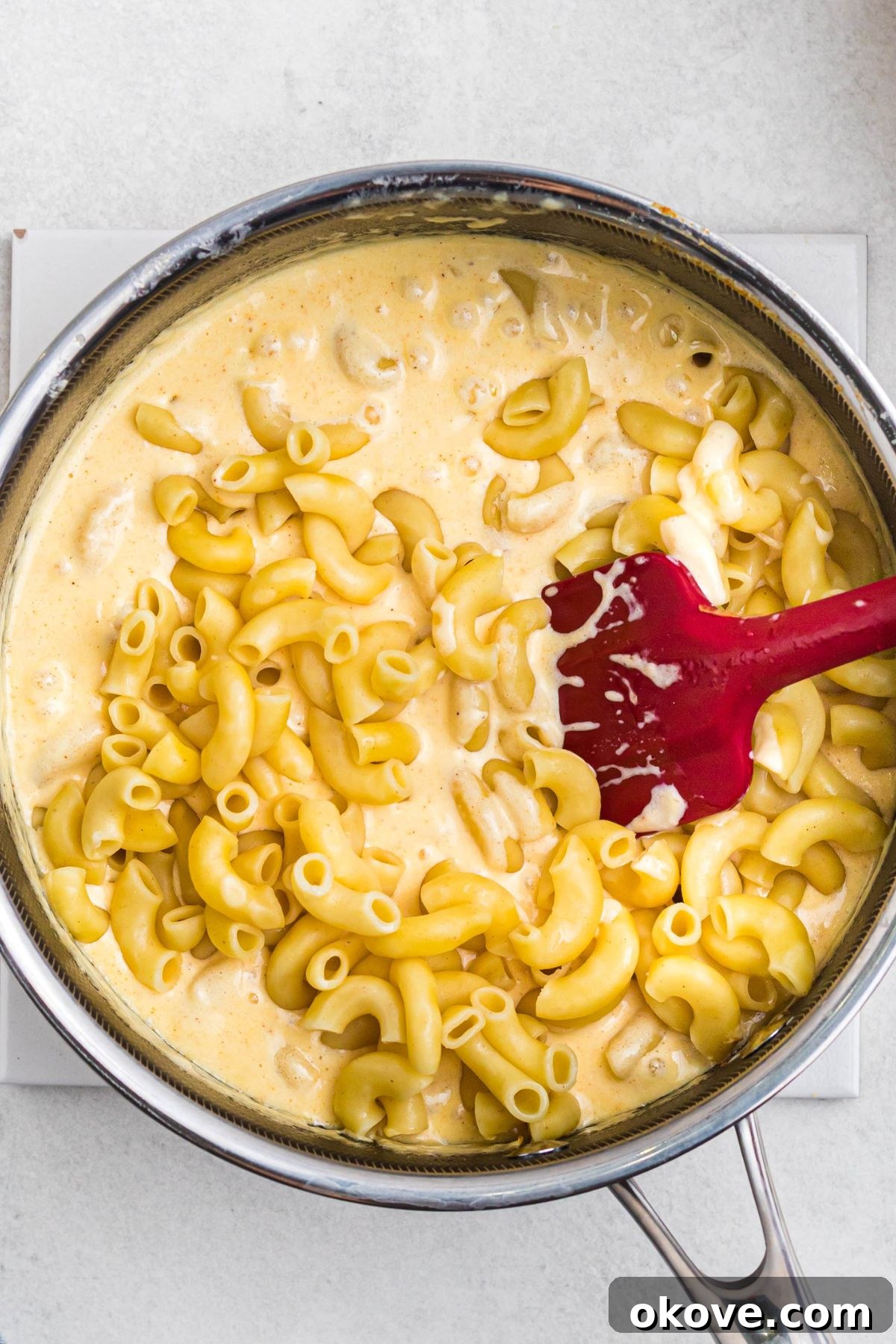 Golden Baked Mac 6 Melted cheese being mixed with elbow macaroni in a saucepan.
