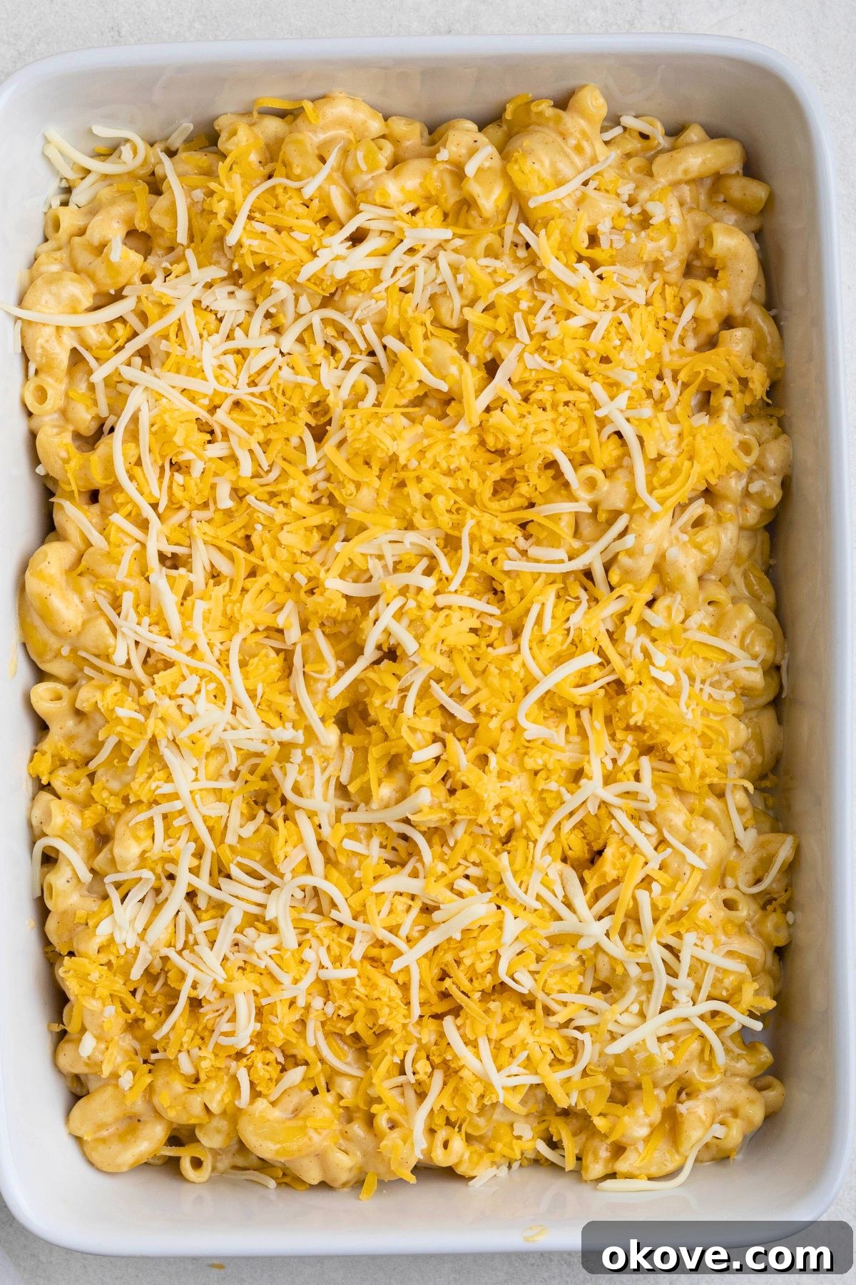 Golden Baked Mac 7 Mac and cheese in a baking dish, topped with shredded cheeses, before baking.