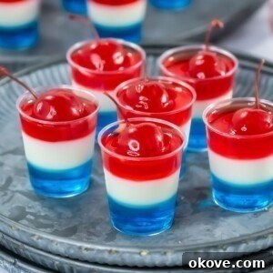 Layered red, white, and blue jello shots displayed beautifully in small shot glasses on a silver serving platter.