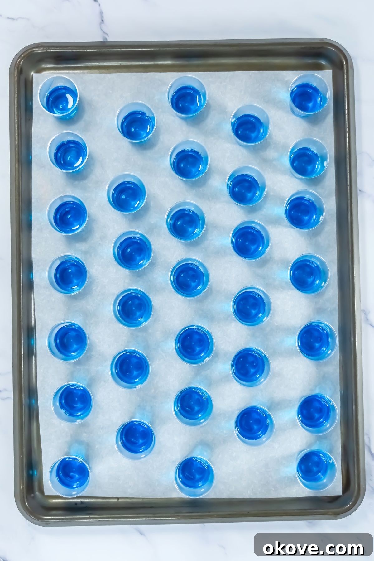 Tri-Color Celebration Shots 5 Small shot glasses arranged on a baking sheet, each filled with the vibrant blue jello mixture, chilling in the refrigerator.