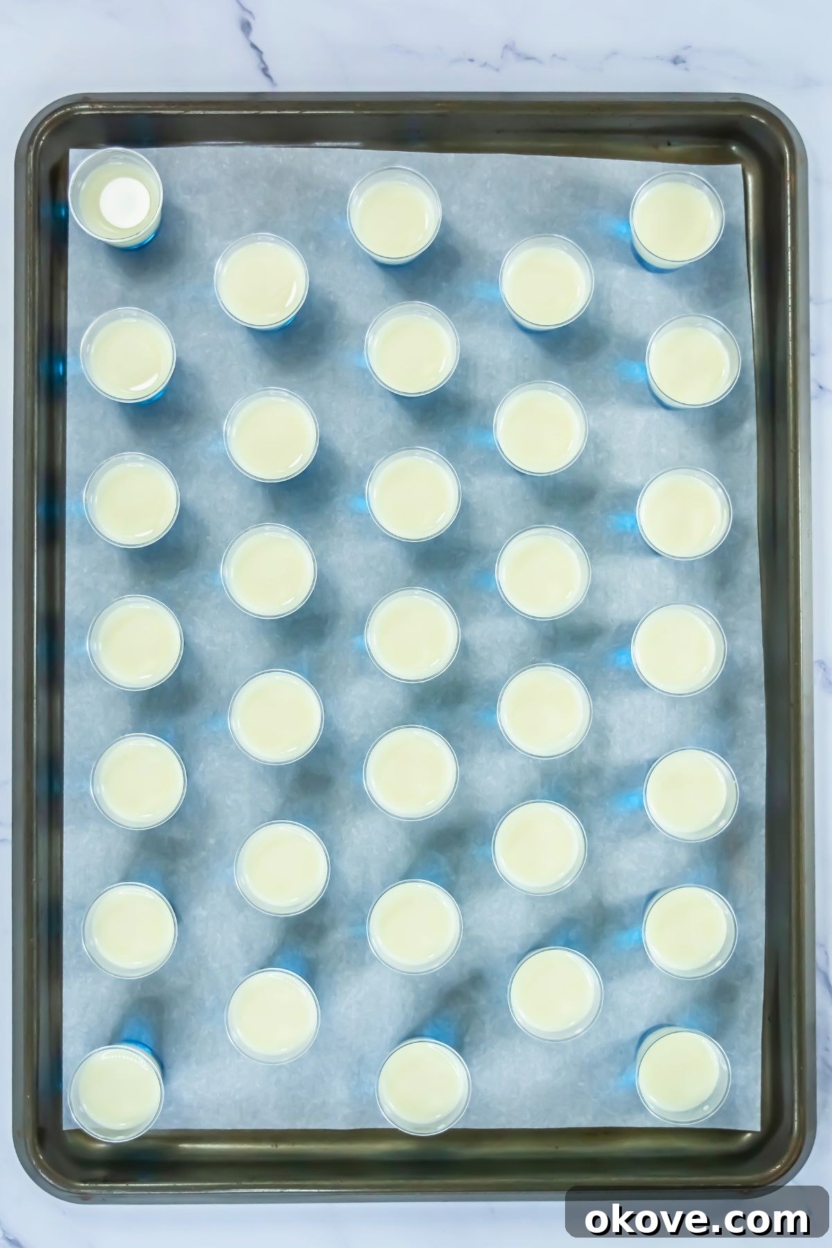 Tri-Color Celebration Shots 7 Small shot glasses on a baking sheet, showcasing the newly poured white gelatin layer over the already set blue gelatin, ready for chilling.