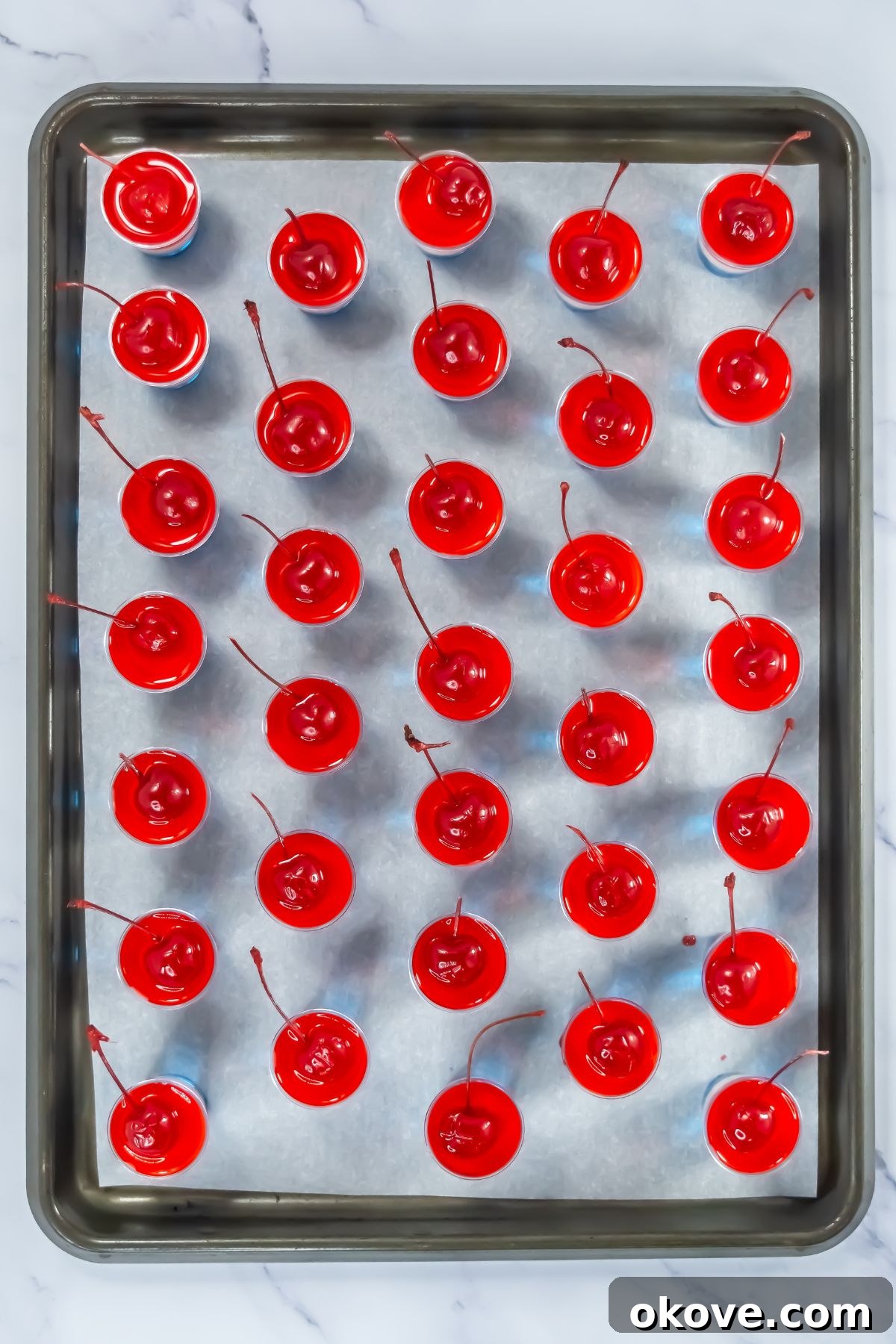 Tri-Color Celebration Shots 9 Jello cups topped with layers of jello and vodka mixture with red on top, on a baking sheet.