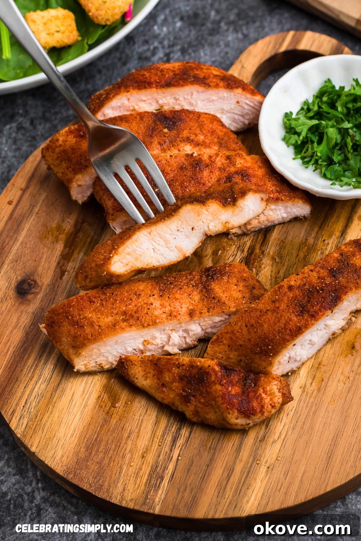 Beautifully smoked, seasoned chicken breasts resting on a small, round cutting board, garnished with fresh parsley flakes.