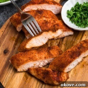Smoked, seasoned chicken on a small, round cutting board, with parsley flakes in a small cutting board.