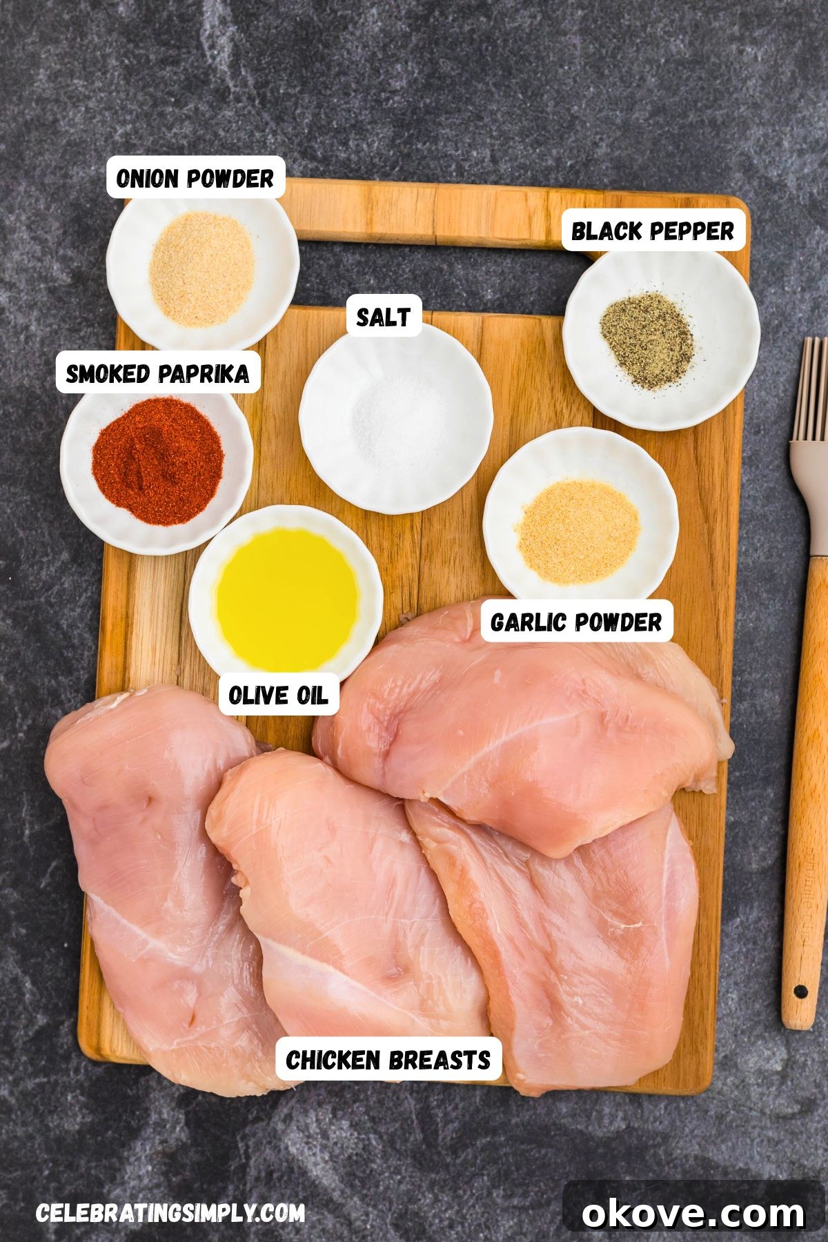 All the dry rub ingredients, including smoked paprika, garlic powder, onion powder, kosher salt, and black pepper, measured into small white dishes next to raw, uncooked chicken breasts on a cutting board.