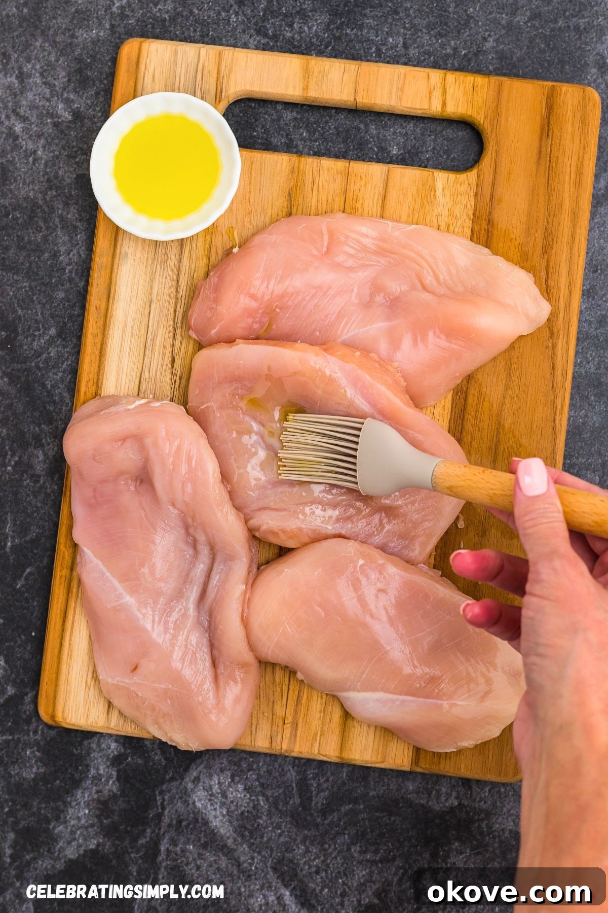 Olive oil being brushed onto uncooked chicken breasts to prepare them for seasoning.