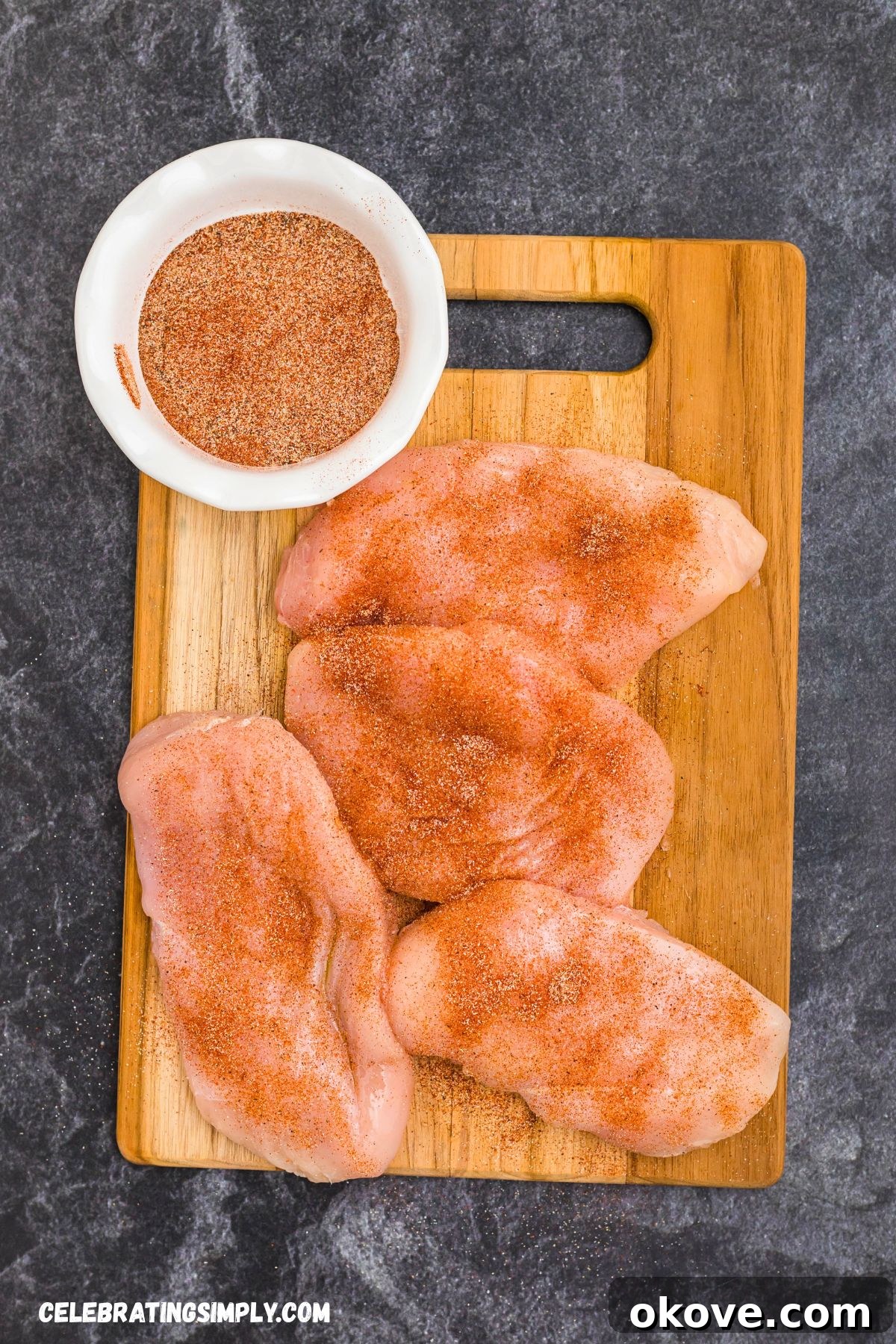 Seasoned chicken breast on a wooden cutting board, ready to be placed on the smoker.