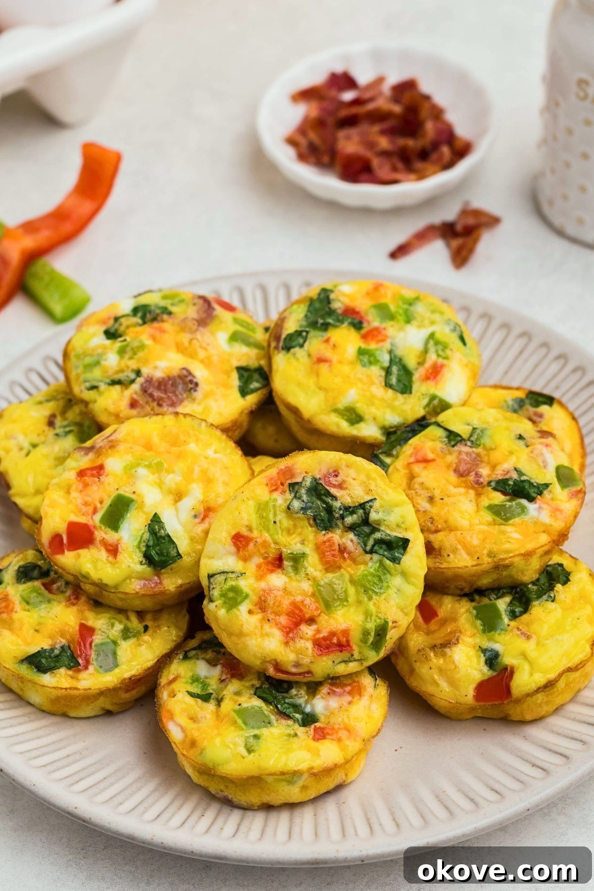 Bright yellow egg bites with red and green chopped bell peppers baked inside, on a round cream plate.