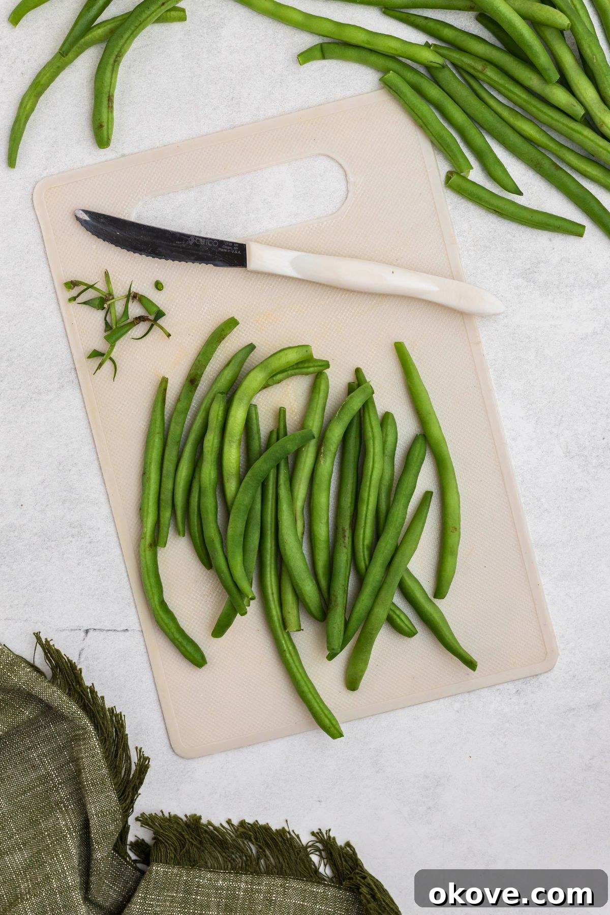 Crispy Roasted Green Beans 4 Fresh green beans being carefully trimmed on a white cutting board, removing the tough ends.