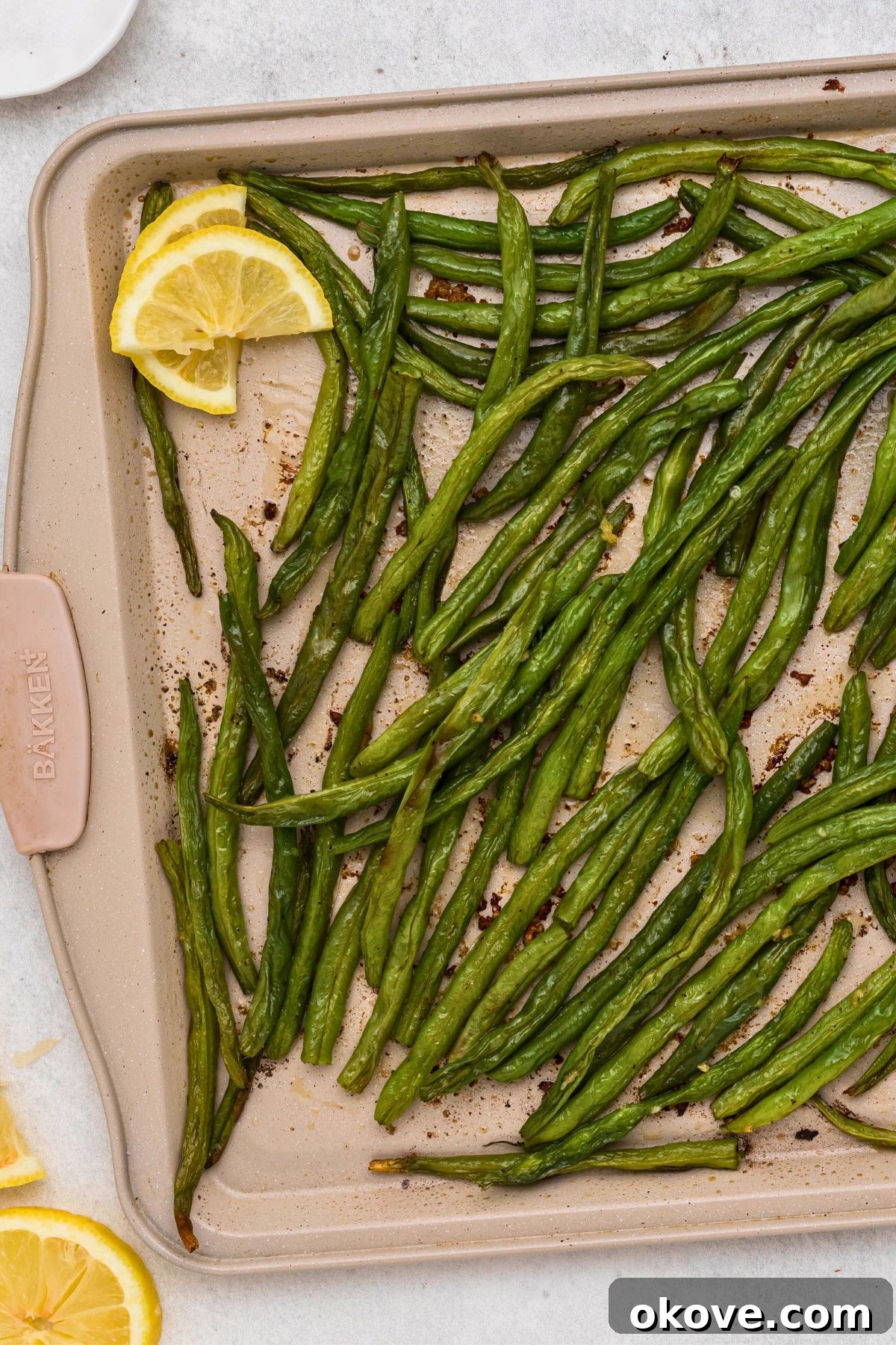 Crispy Roasted Green Beans 7 Freshly roasted green beans on a baking sheet being finished with a drizzle of fresh lemon juice, ready for serving.