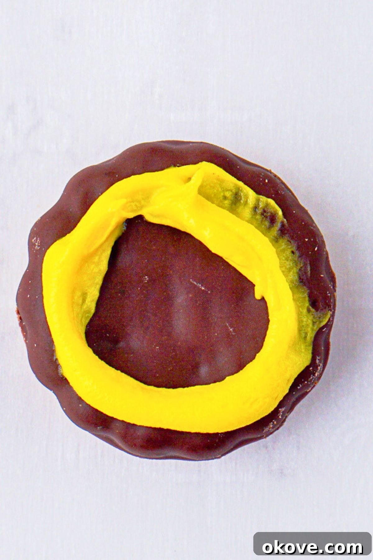 Dessert Burgers 5 A chocolate fudge mint cookie topped with neatly piped rings of yellow icing, resembling mustard, ready for the next layer of the hamburger cookie assembly.