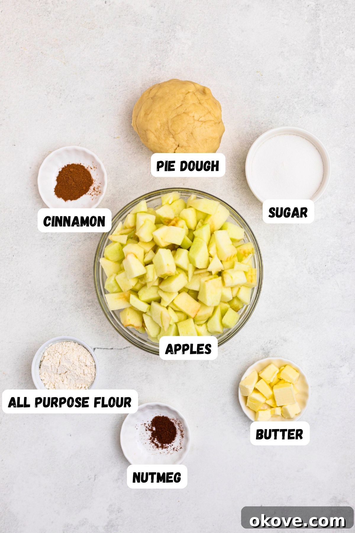 Ingredients needed to make apple pie, measured into small bowls, on a white marble table. 