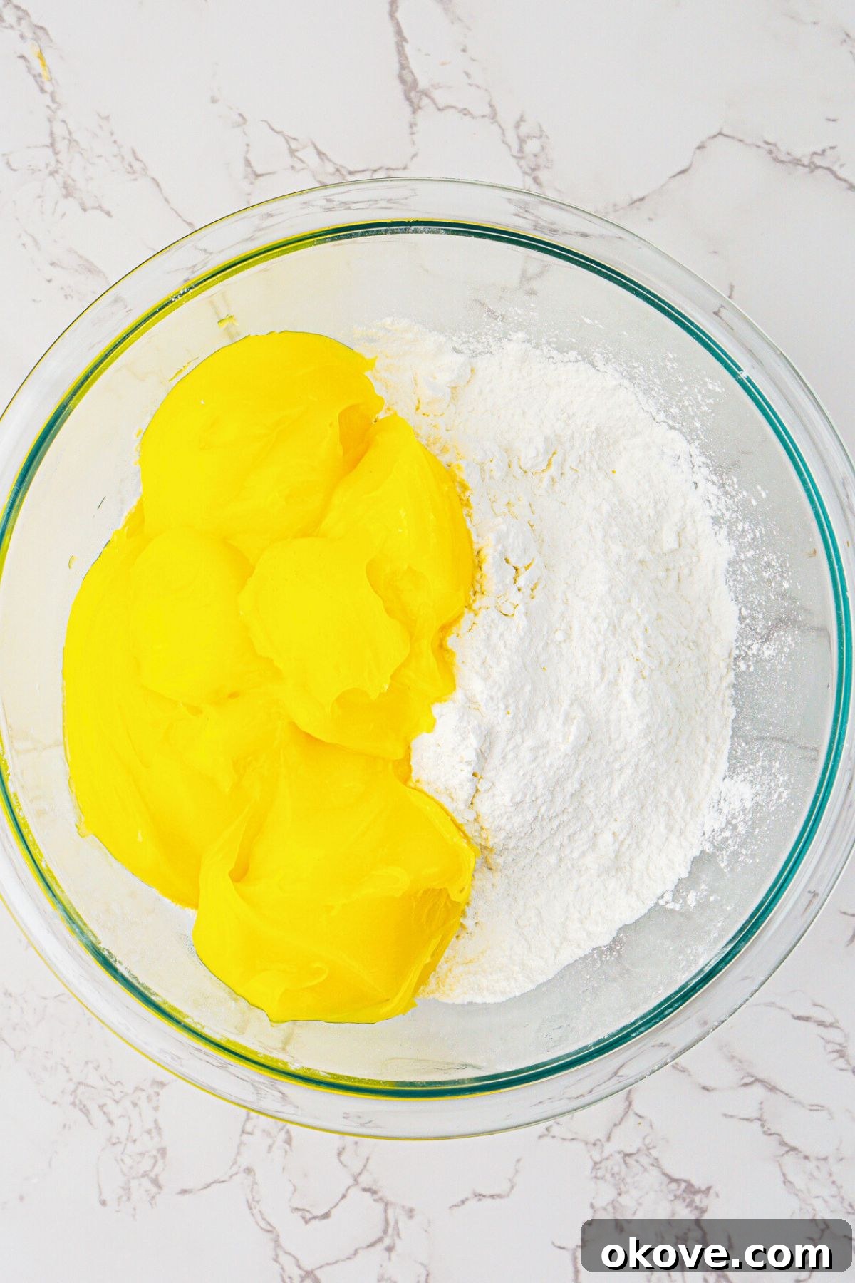 Effortless Two-Ingredient Lemon Bars 4 Cake mix and lemon pie filling being mixed together in a clear glass bowl. The initial mixing step for 2-ingredient lemon bars.