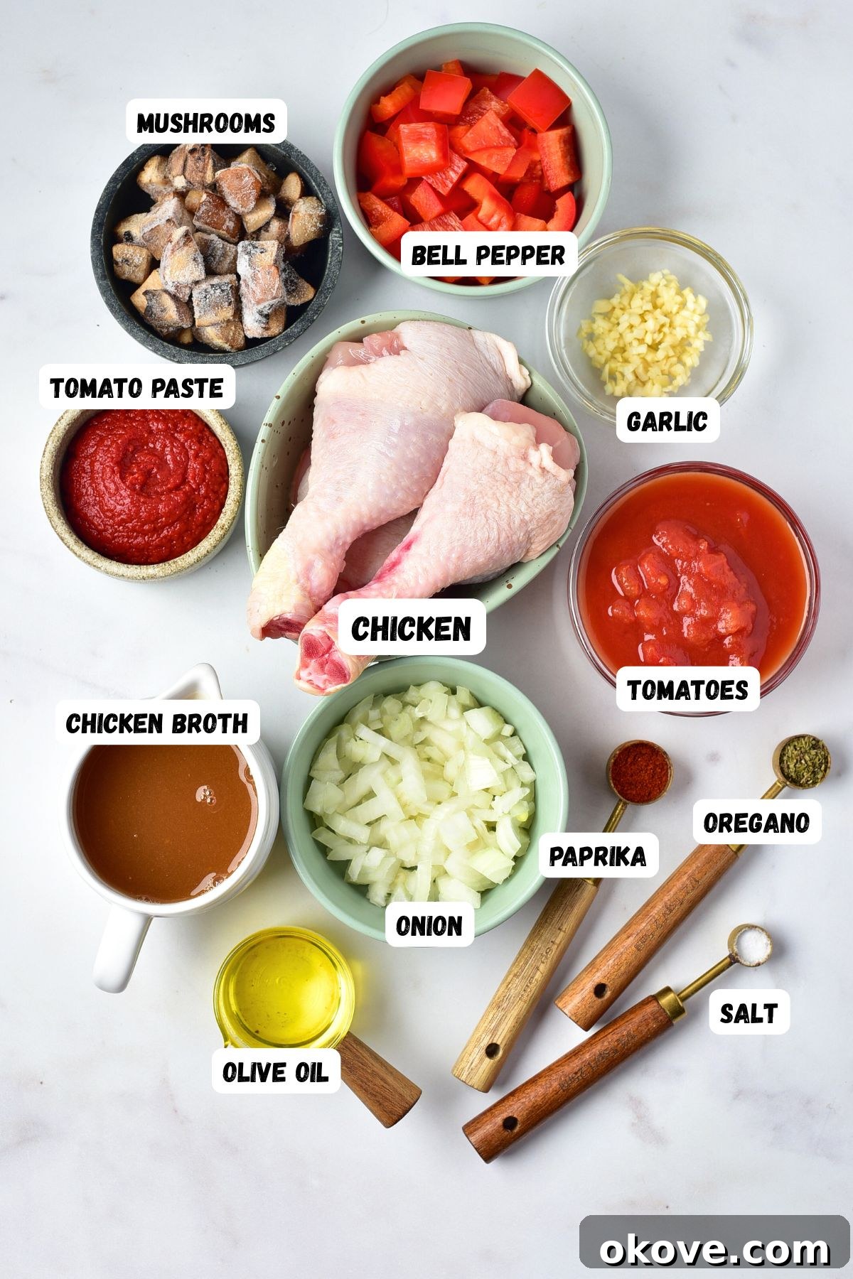 Deliciously Simple Slow Cooker Chicken Cacciatore 3 Assorted fresh ingredients for chicken cacciatore including seasoned bone-in chicken pieces, chopped mushrooms, onion, minced garlic, bell pepper, canned diced tomatoes, tomato paste, and a selection of spices and herbs, neatly arranged on a white marble table.
