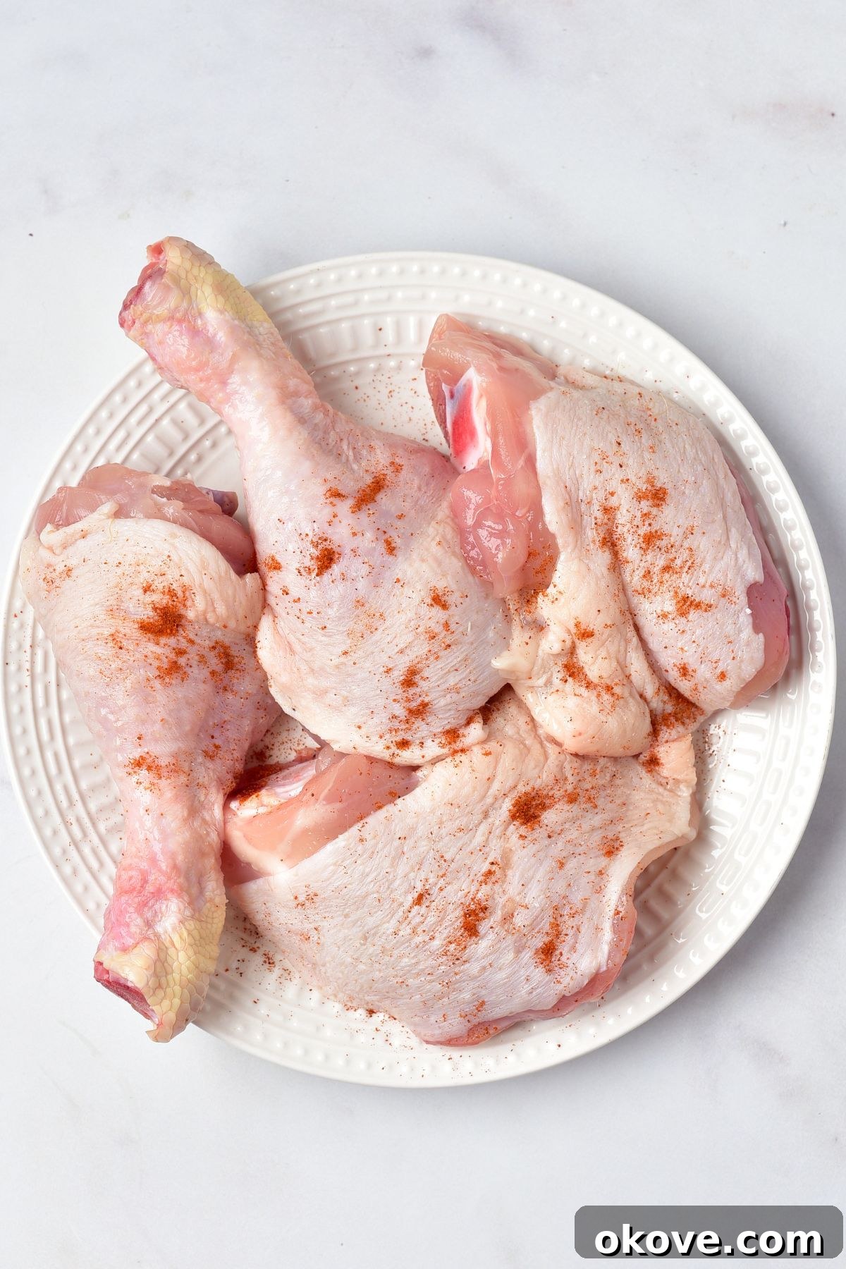 Deliciously Simple Slow Cooker Chicken Cacciatore 4 Uncooked chicken pieces, seasoned generously with salt and paprika, arranged on a clean white plate on a marble surface, ready for the slow cooker.