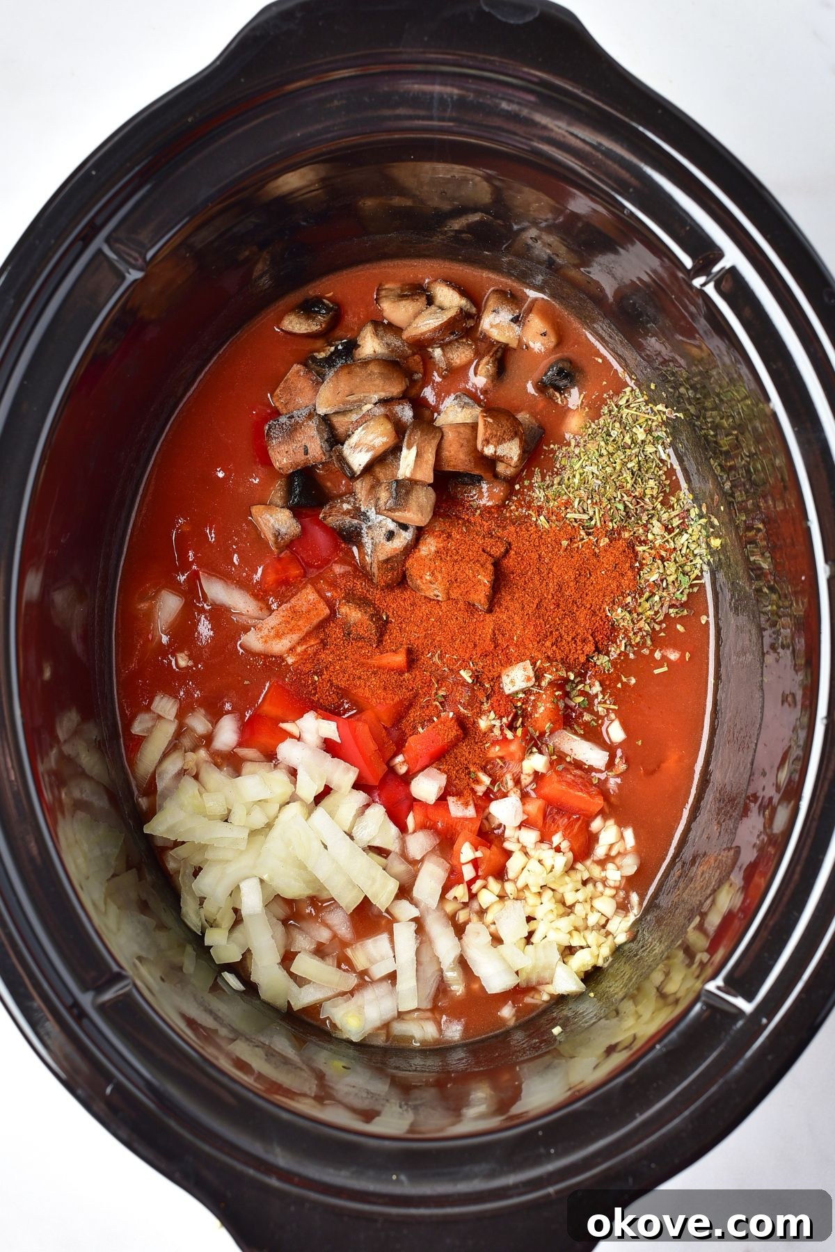 Deliciously Simple Slow Cooker Chicken Cacciatore 5 A slow cooker pot filled with a vibrant mix of chopped mushrooms, finely diced onion, minced garlic, red bell pepper, canned diced tomatoes, chicken broth, tomato paste, olive oil, and dried oregano, before being mixed together to form the sauce base.