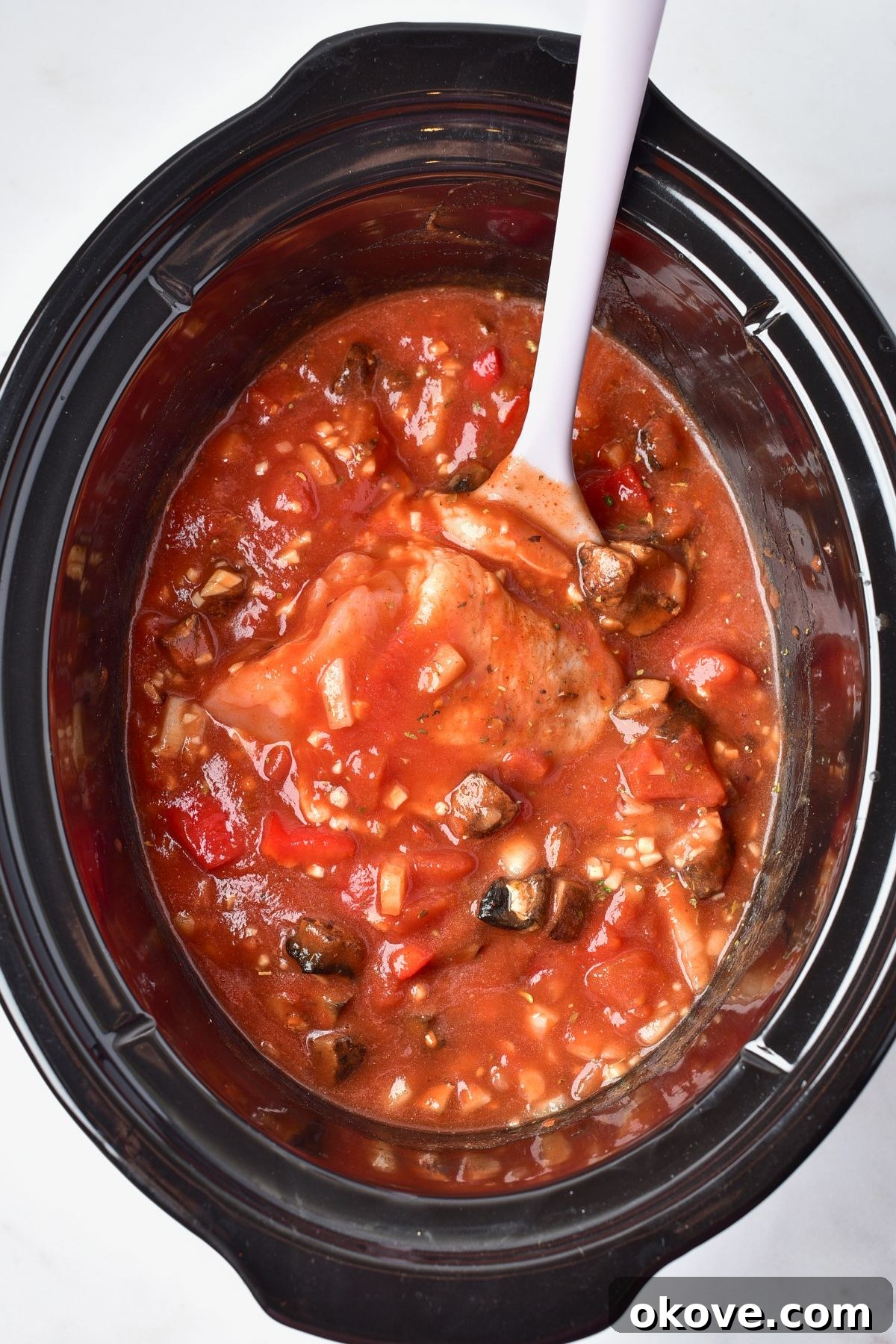 Deliciously Simple Slow Cooker Chicken Cacciatore 6 Seasoned uncooked chicken pieces carefully placed into the slow cooker, nestling amongst the rich tomato and vegetable sauce, ready for cooking.