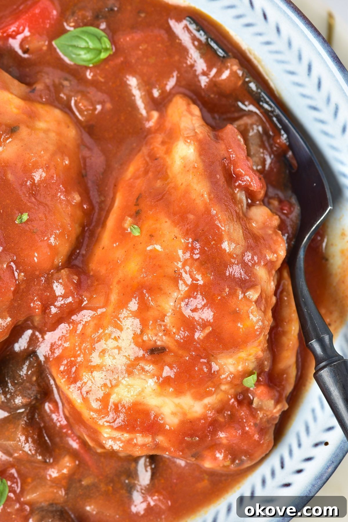 Deliciously Simple Slow Cooker Chicken Cacciatore 8 A close-up shot of a serving of slow cooker chicken cacciatore in a white bowl, showcasing the tender chicken, rich tomato sauce, and colorful vegetables, garnished with fresh herbs.
