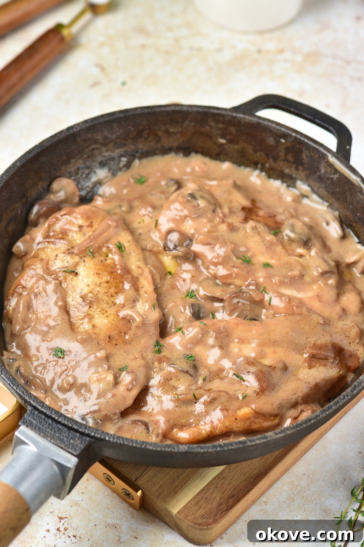Chicken and sauce thickened in a black skilled, on a wooden cutting board.