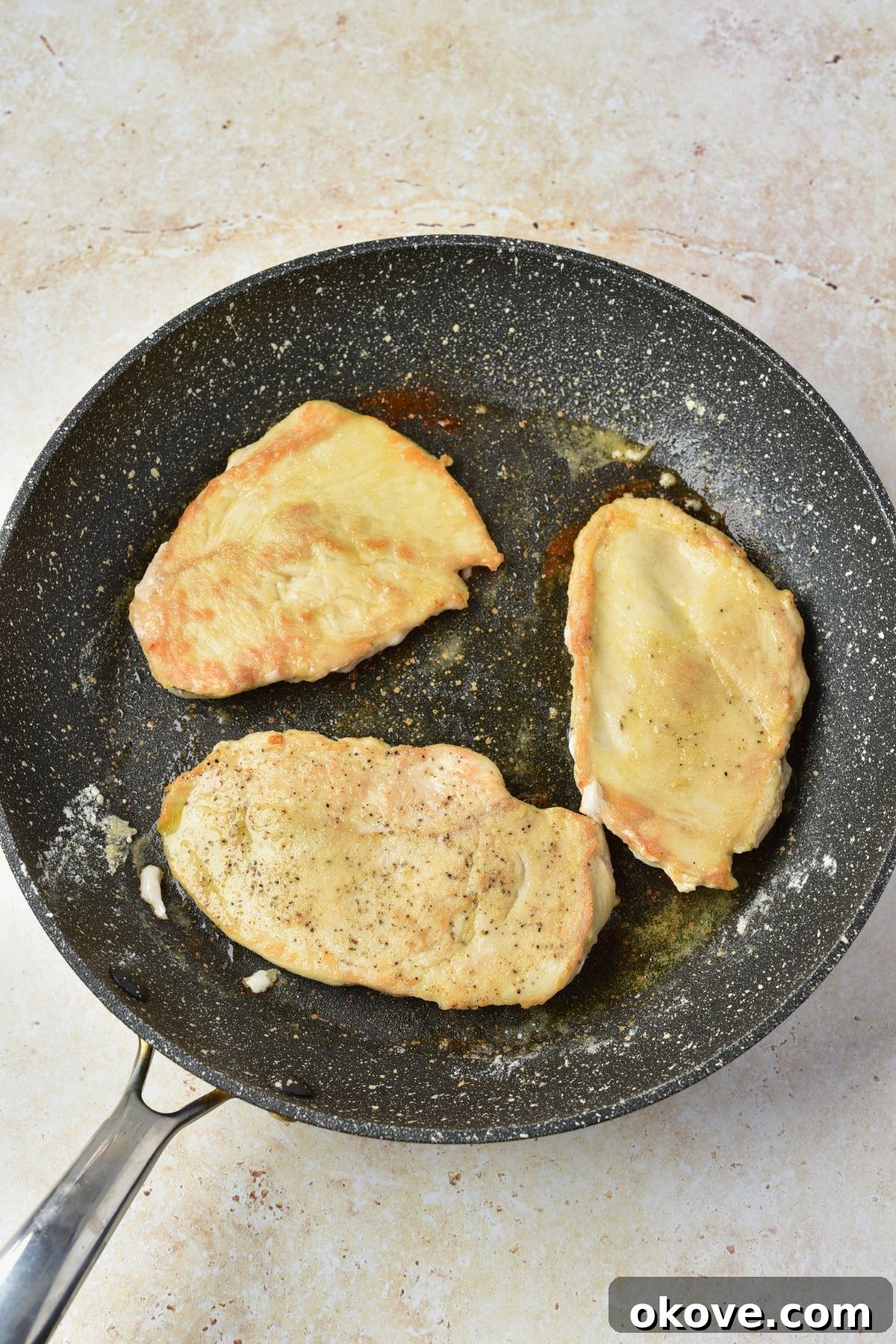 Chicken being seared in a large skilled, before having other ingredients added to make chicken marsala.