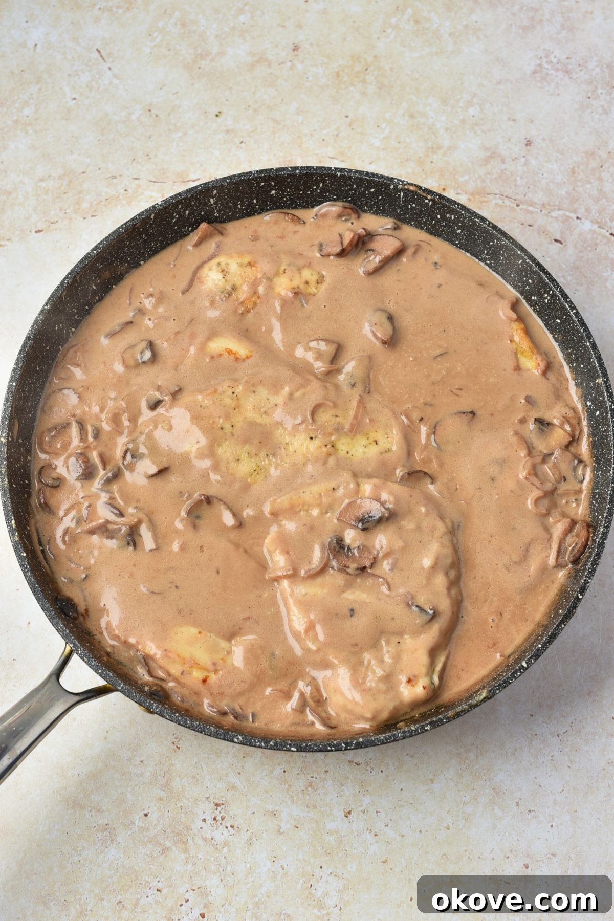 Chicken in skillet with creamy sauce, waiting for sauce to thicken.