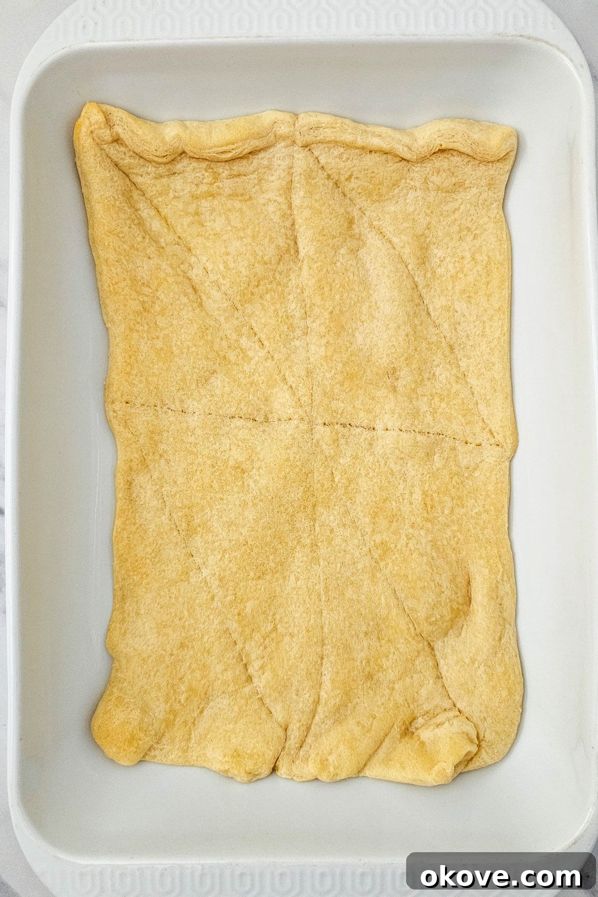 Homestyle Chicken Pot Pie Bake 4 Golden baked crescent roll crust at the bottom of a white rectangular baking dish.