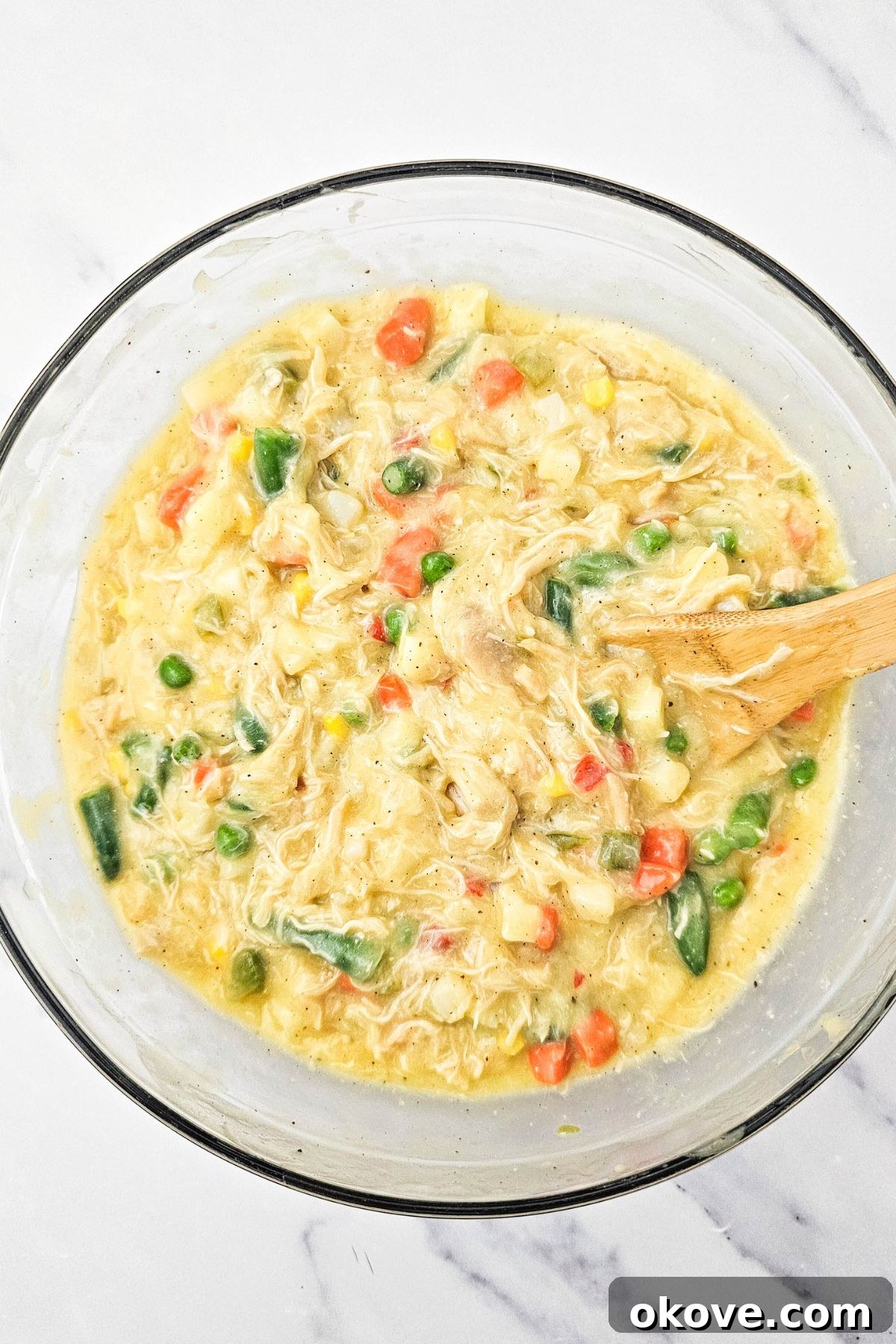 Homestyle Chicken Pot Pie Bake 5 Creamy pot pie filling with shredded chicken, mixed vegetables, and a rich sauce in a clear glass mixing bowl.