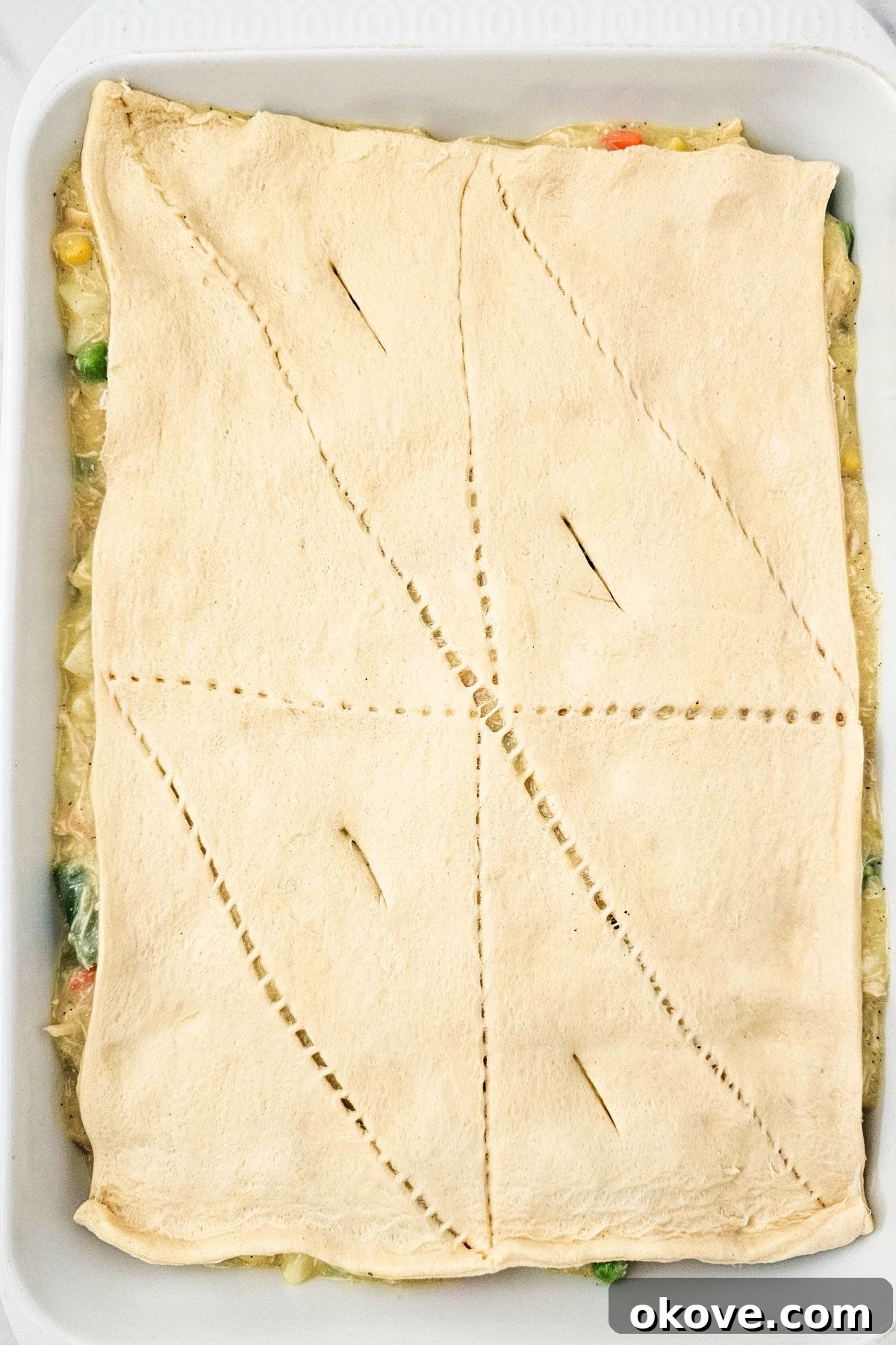 Homestyle Chicken Pot Pie Bake 7 Unbaked crescent roll dough covering the pot pie filling in the casserole dish, with seams pinched and small slits cut for ventilation.